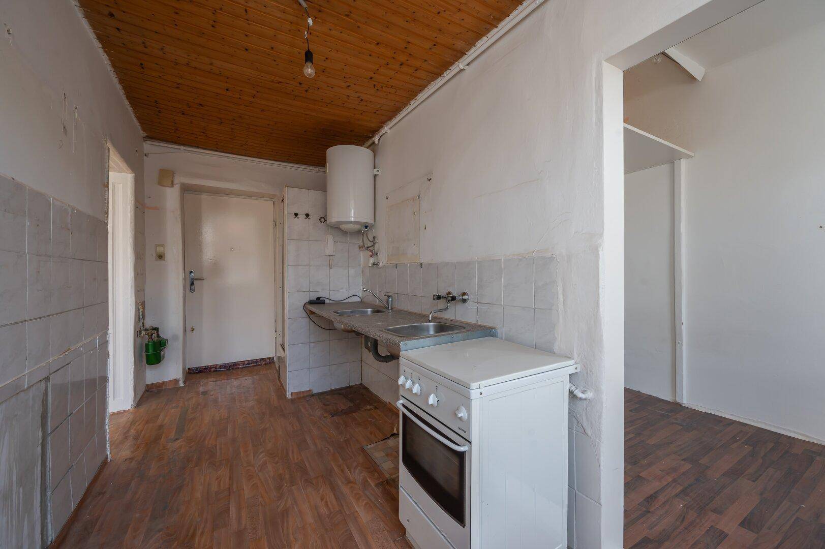 Renovierungsbedürftige Küche mit einfacher Ausstattung, Holzdecke und gefliesten Wänden.