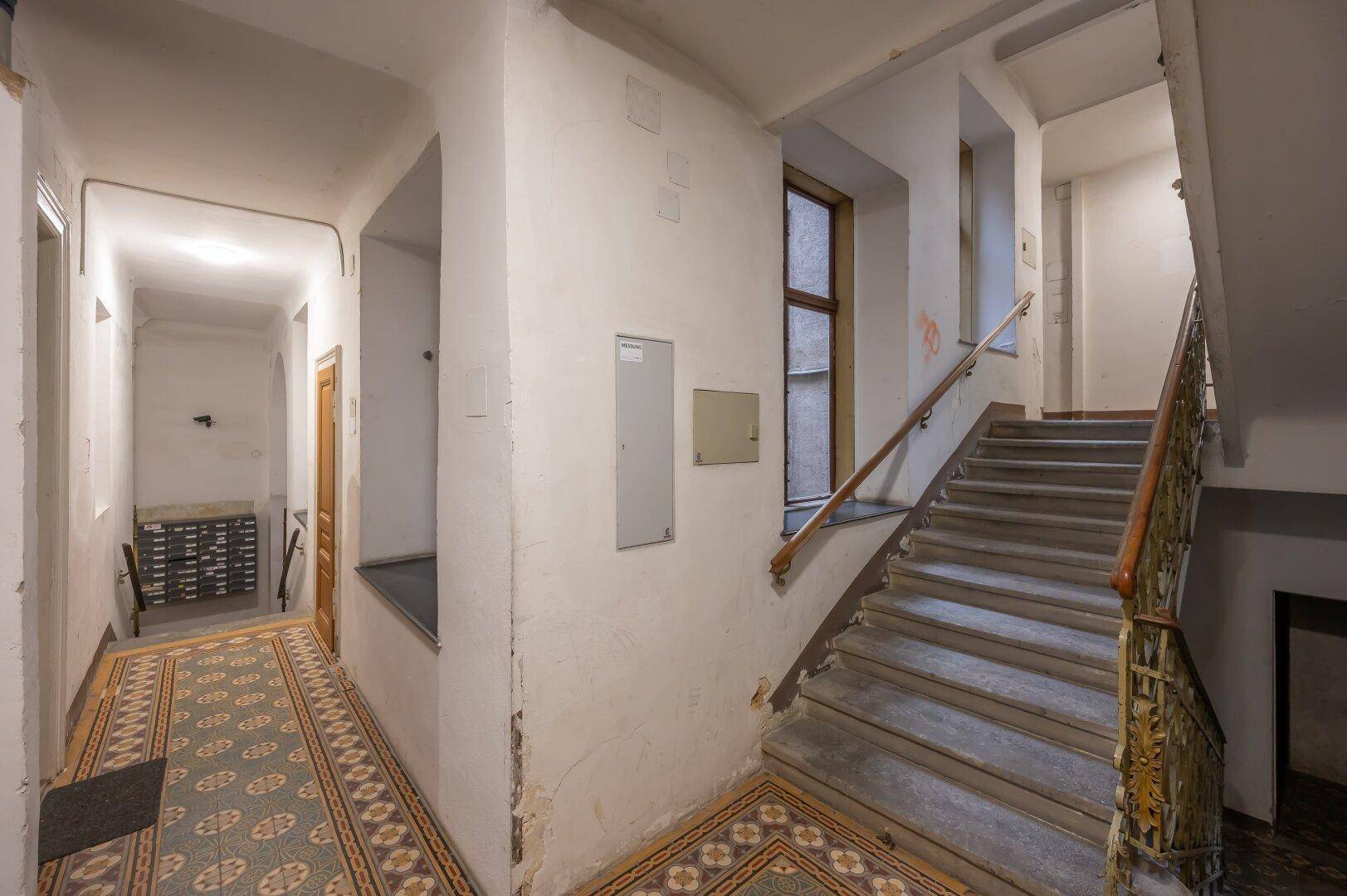 Geräumiges Treppenhaus in einem Altbau mit breiten Stufen und dekorativen Bodenfliesen.