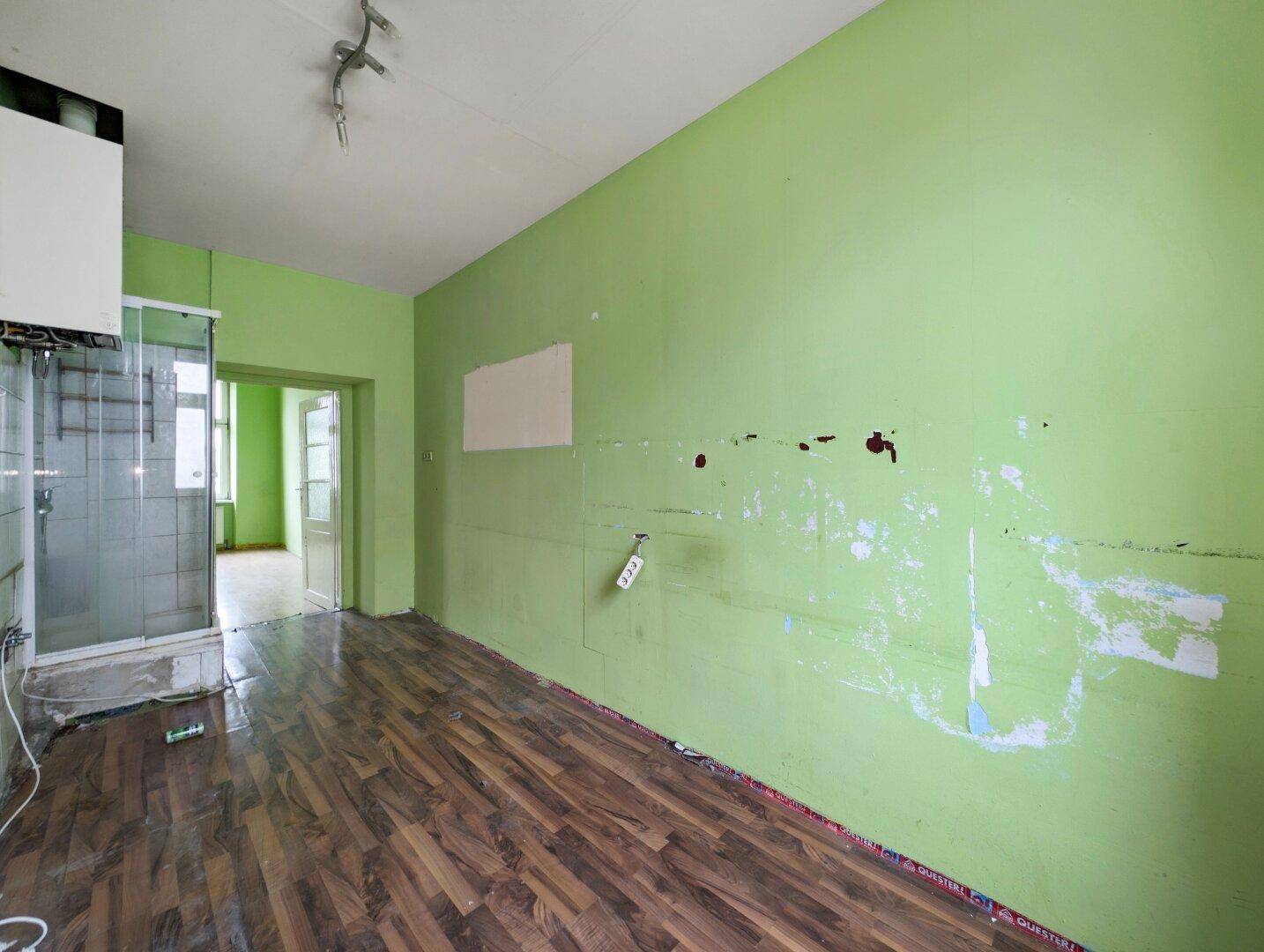 Leerer Raum mit grünen Wänden, dunklem Holzboden und einer sichtbaren Duschkabine.