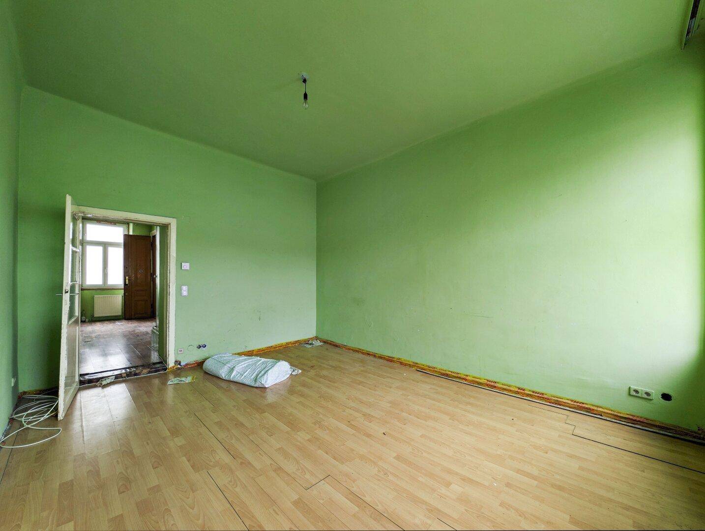 Unmöbliertes Zimmer mit grünen Wänden, Holzboden und offener Tür zu einem weiteren Raum.