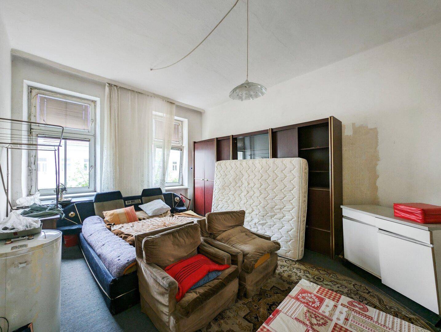 Verwahrlostes Wohnzimmer mit alten Sesseln, Sofa und einer Matratze, die an der Wand lehnt.