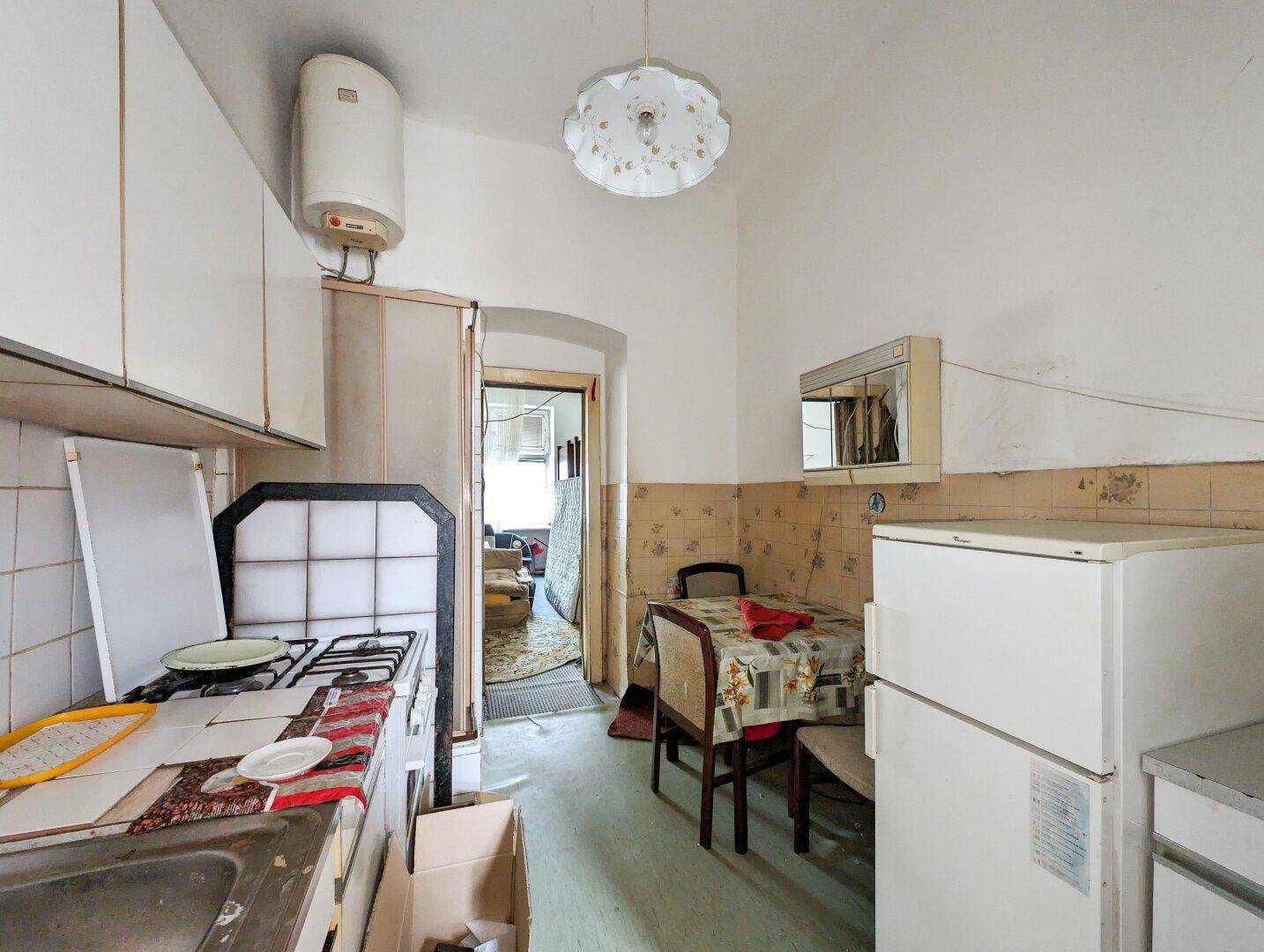 Einfache Küche in altem Zustand mit kleinem Esstisch, Kühlschrank und Gasherd.