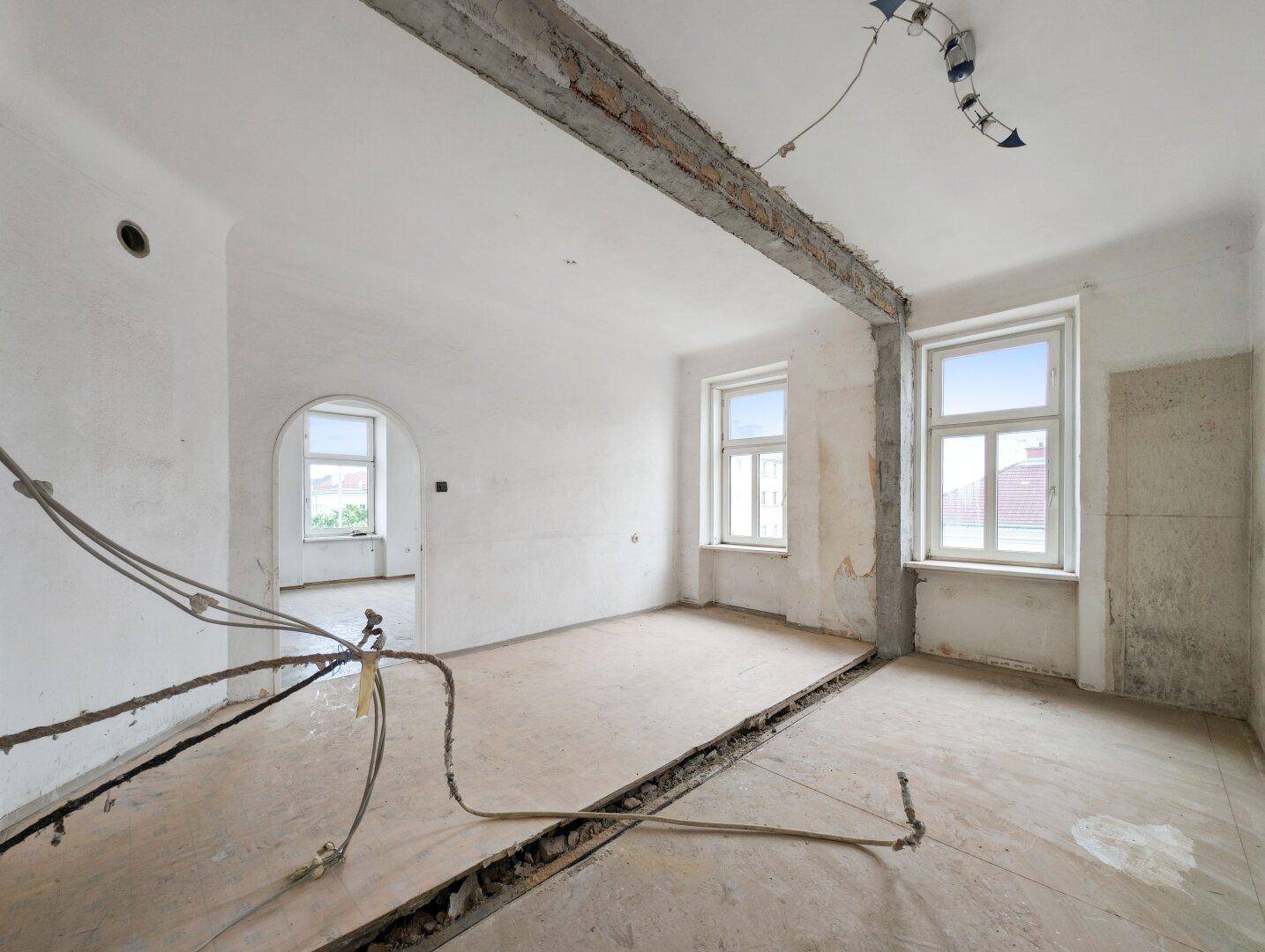 Renovierungsbedürftiges Zimmer mit freigelegtem Deckenbalken und entfernten Bodenbelägen.