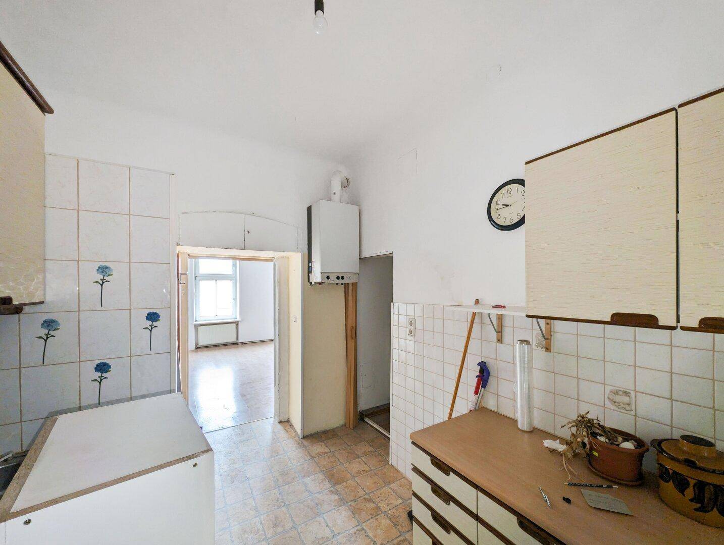 Ältere Küche mit gefliesten Wänden, einfachen Schränken und Gastherme, benötigt Modernisierung.