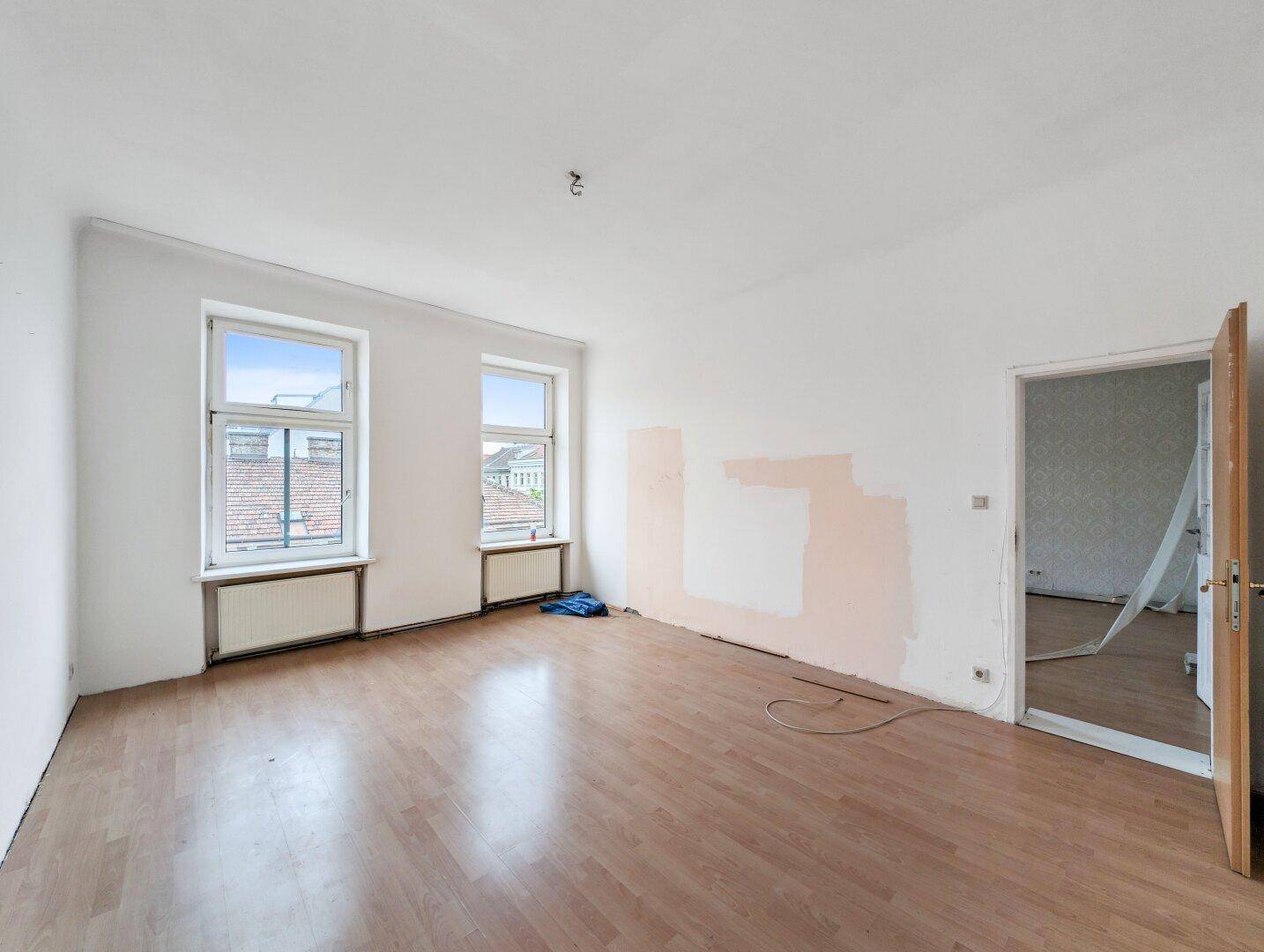 Helles Wohnzimmer mit Laminatboden und teilweise entfernter Tapete, ideal zur Neugestaltung.