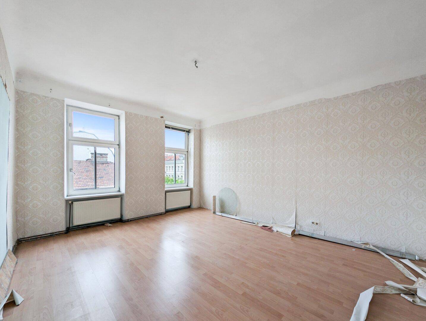 Großes Zimmer mit Laminatboden und Resten alter Tapete, bereit für eine Modernisierung.