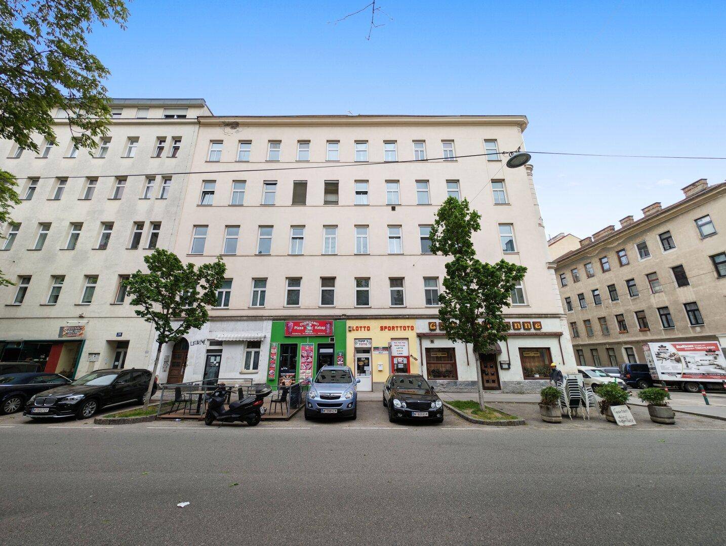 Mehrstöckiges Wohngebäude mit Geschäften im Erdgeschoss an einer belebten Stadtstraße.