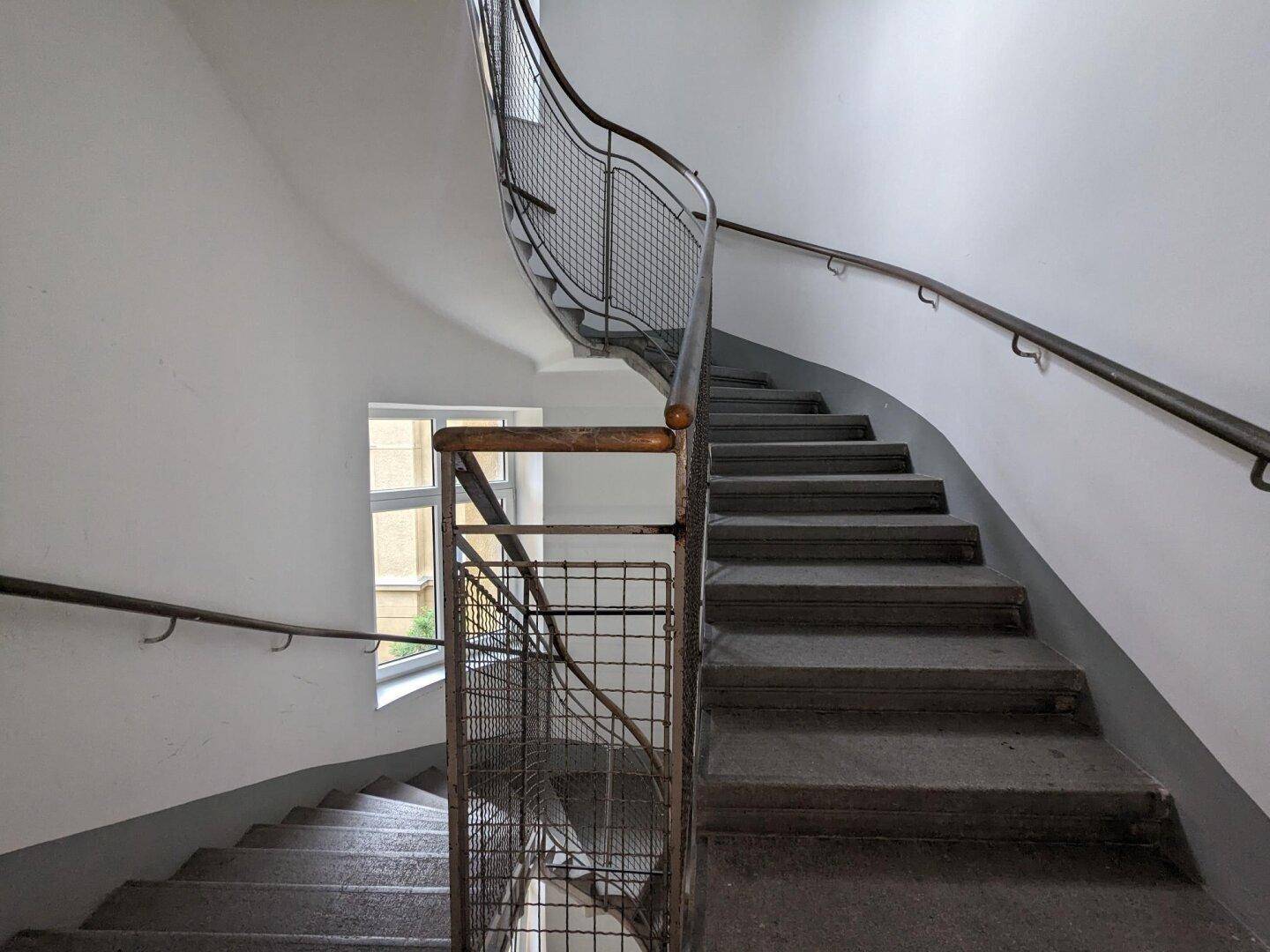 Historisches Treppenhaus mit Steinstufen, schmiedeeisernem Geländer und Fenster.