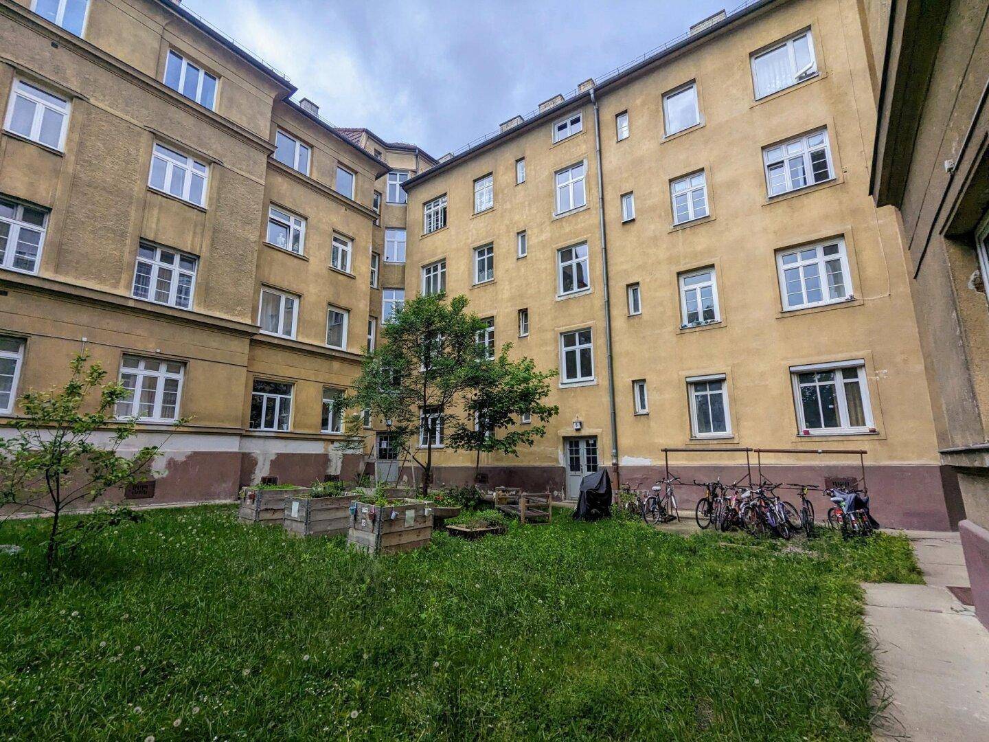 Begrünter Innenhof eines Wohngebäudes mit Hochbeeten und Fahrradabstellplätzen.