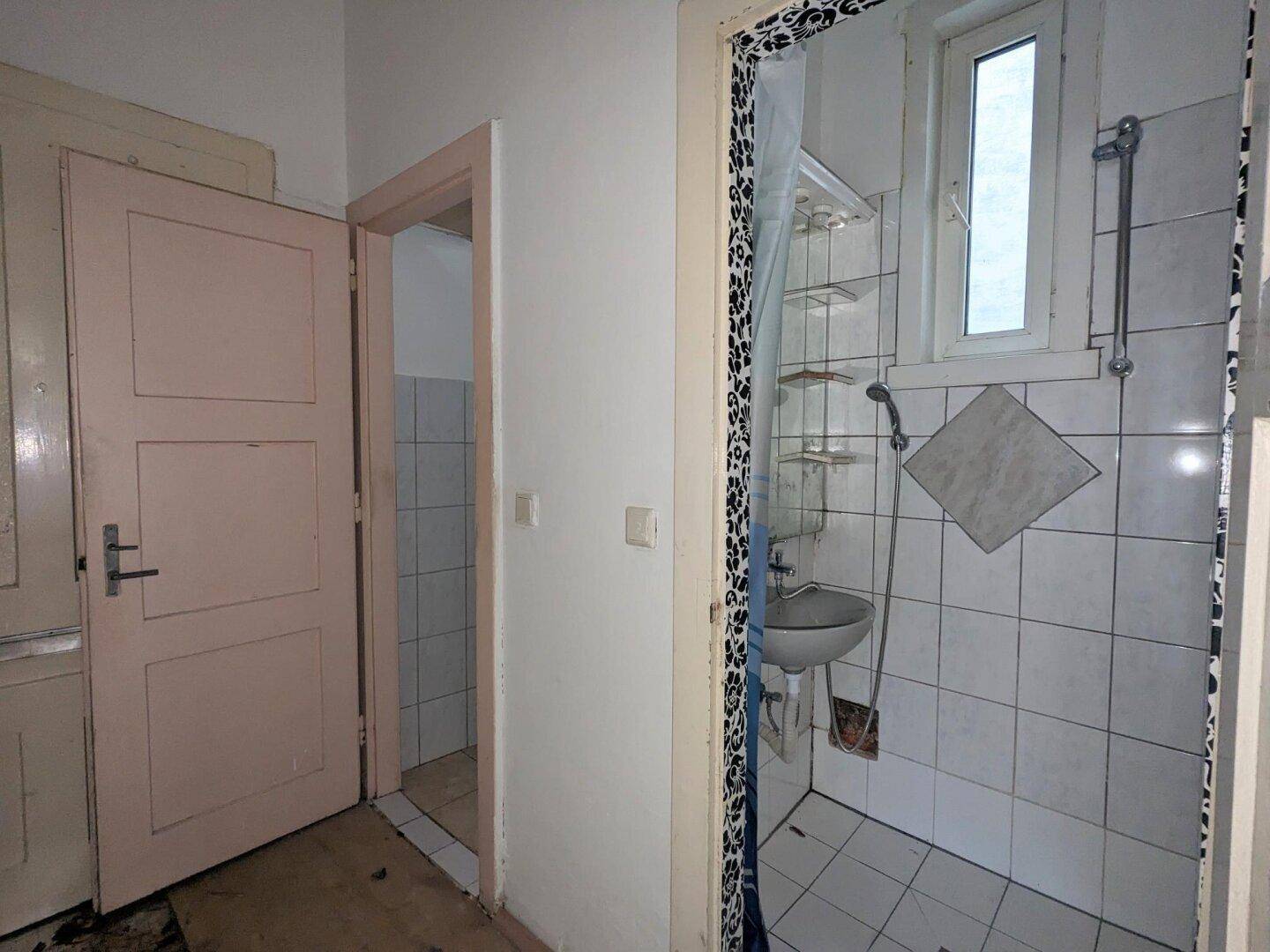 Kleines Badezimmer mit Dusche, Waschbecken, Fenster und weißen Fliesen.