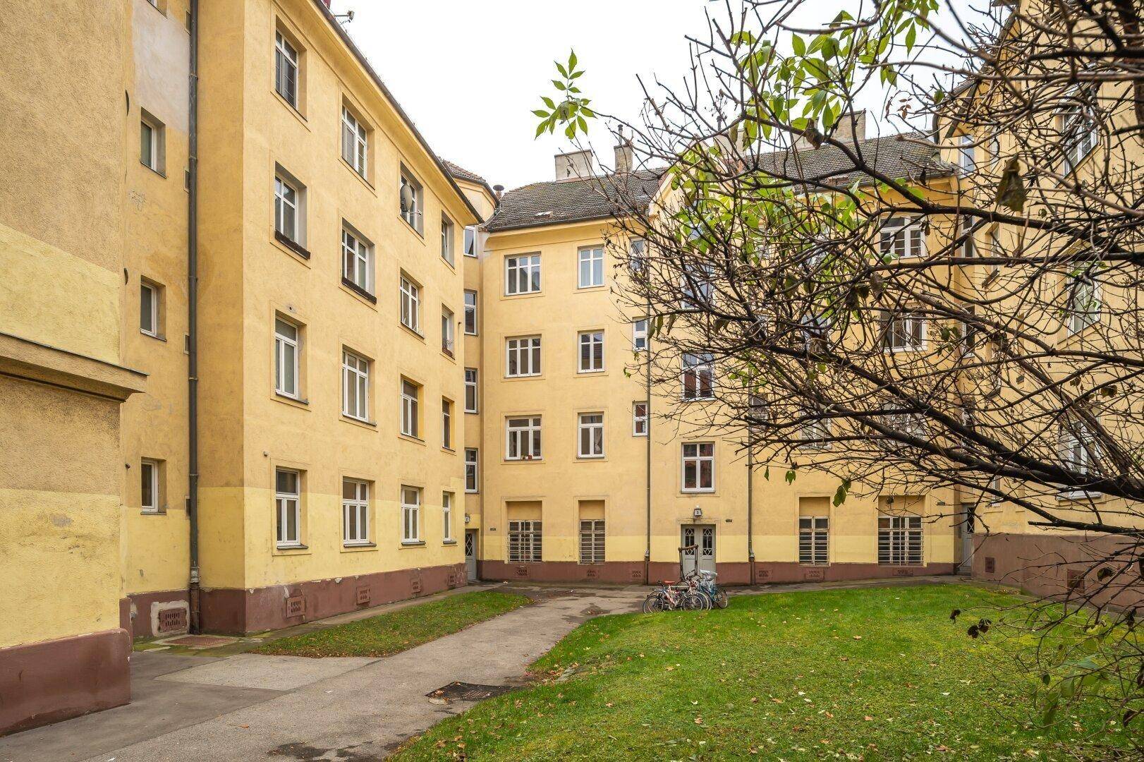 Innenhof eines Mehrfamilienhauses mit gelber Fassade, Grünfläche und Bäumen.