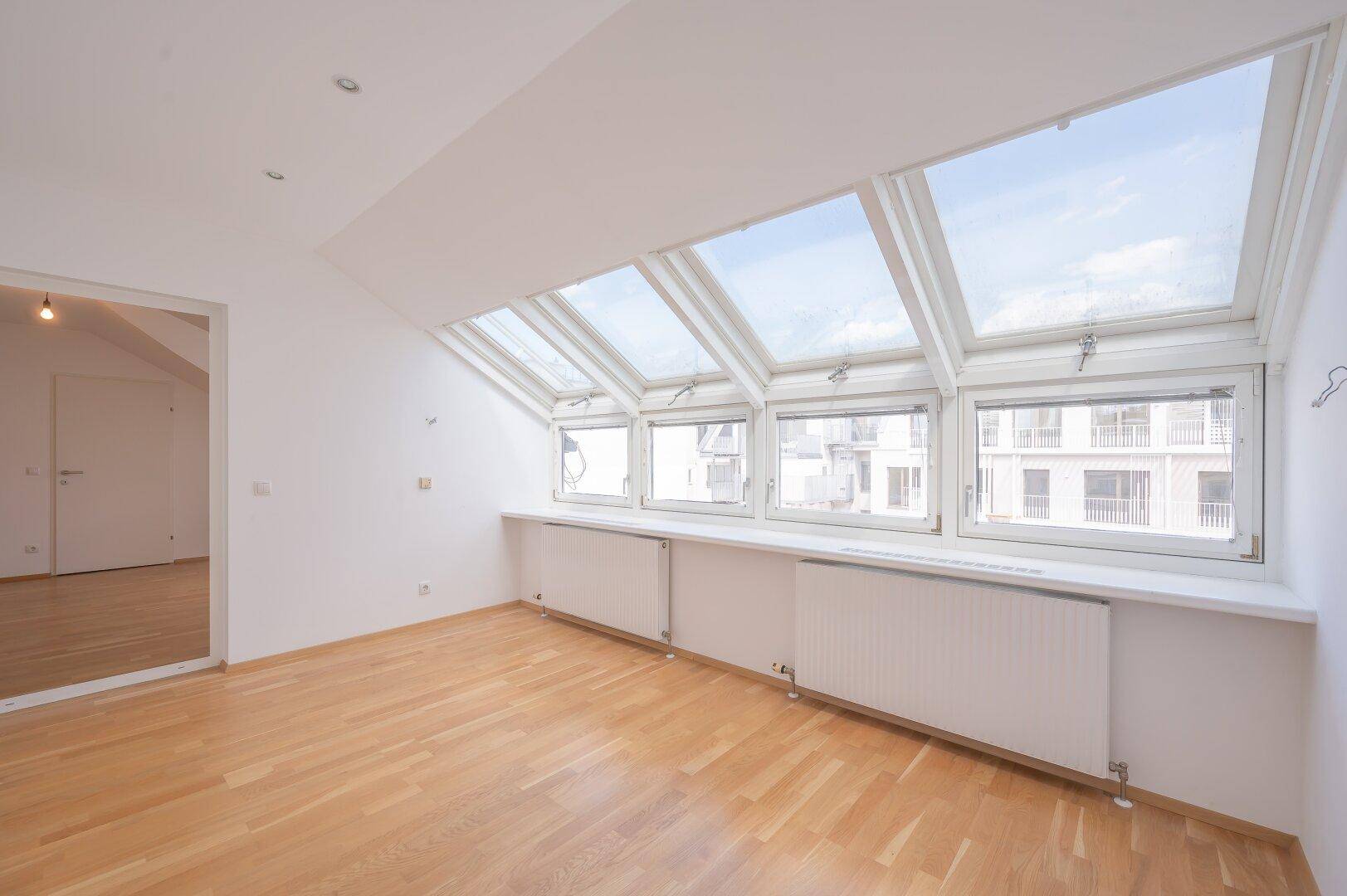Heller Wohnbereich mit Parkettboden und großen Dachfenstern, die viel Tageslicht bieten.
