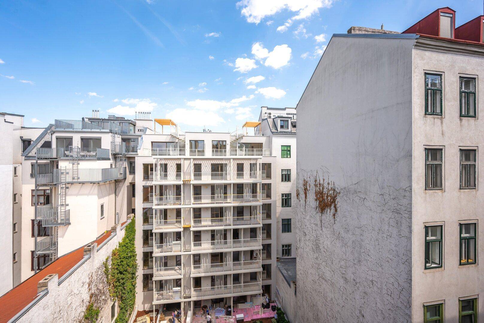 Blick auf die Rückseite eines Wohnkomplexes mit mehreren Balkonen und Terrassen.