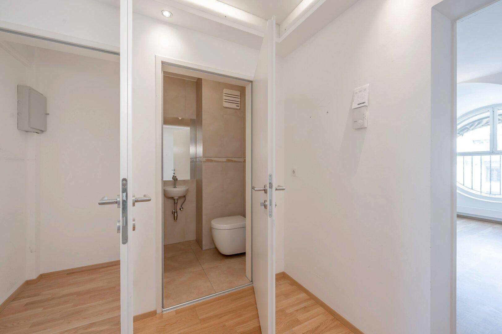 Kleines Gäste-WC mit Waschbecken, Toilette und hellen Fliesen.