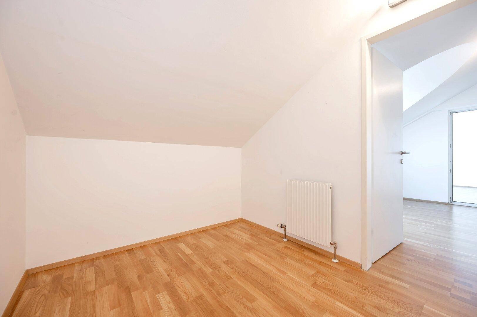 Kleiner Raum mit Dachschräge, Parkettboden und Heizkörper, ideal als Arbeits- oder Kinderzimmer.