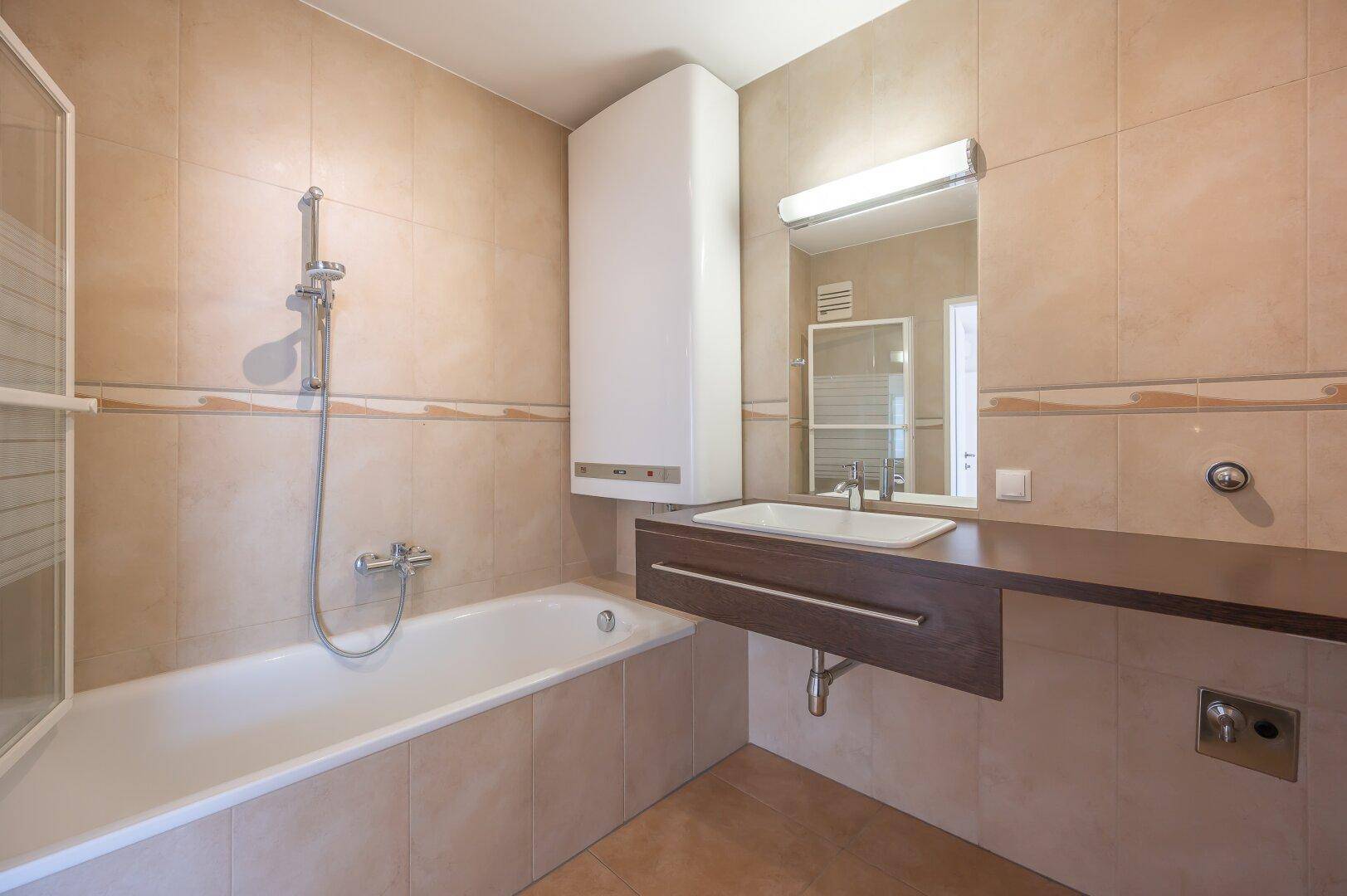 Badezimmer mit Badewanne, Duschfunktion, Waschbecken und beigefarbenen Fliesen.