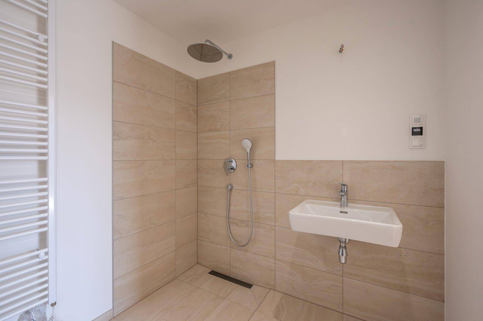 Modernes Badezimmer mit ebenerdiger Dusche, kleinem Waschbecken und beheiztem Handtuchhalter.
