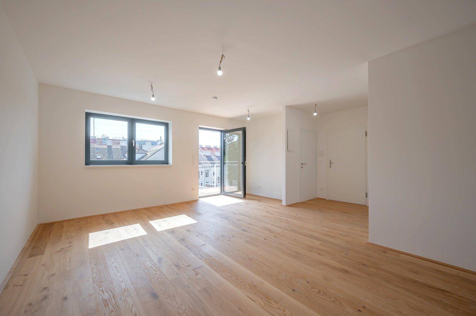 Geräumiger, heller Raum mit Eichenparkettboden, großen Fenstern und Zugang zu einem Balkon.