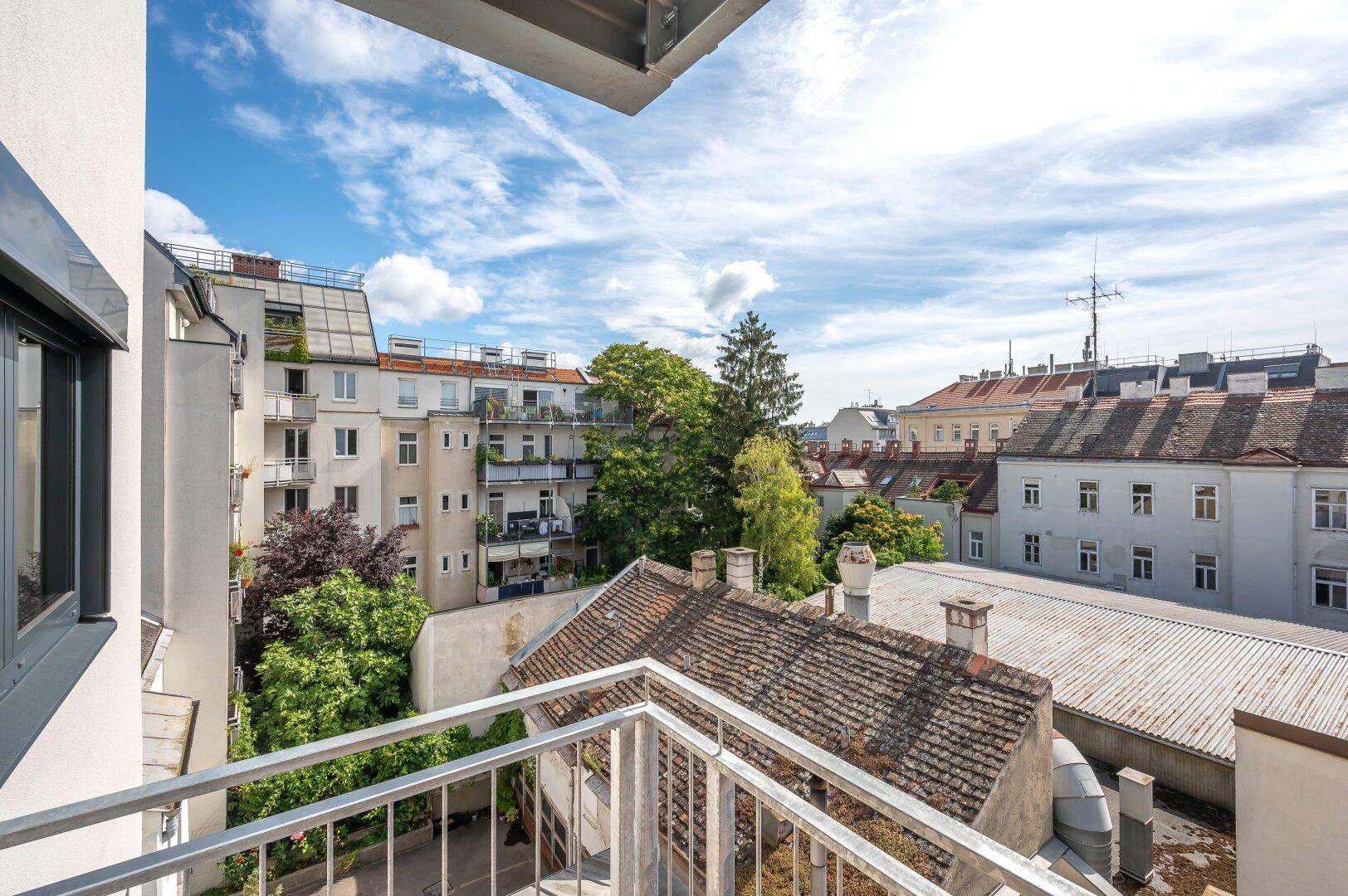 Balkon mit Holzboden und Blick auf die umliegenden Gebäude und grüne Bäume.