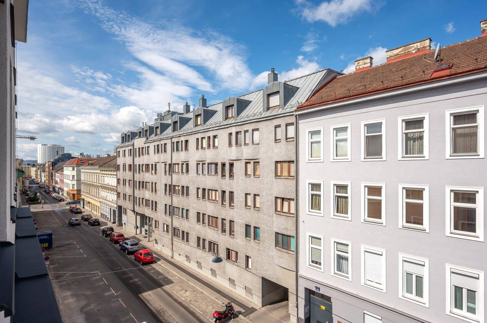 Weitblick über eine städtische Straße mit geparkten Autos und umliegenden Wohngebäuden.