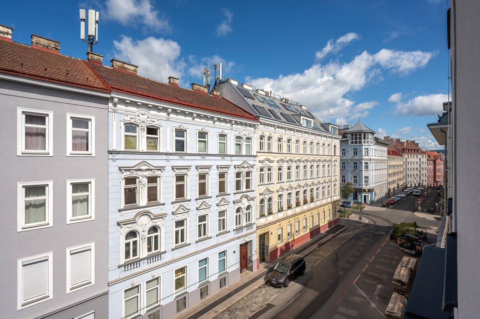 Panoramablick auf eine belebte Stadtstraße mit historischen und modernen Wohngebäuden.