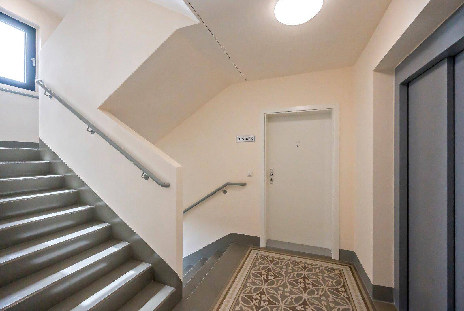 Helles Treppenhaus mit Aufzug und modernem Bodenbelag in einem Mehrfamilienhaus.