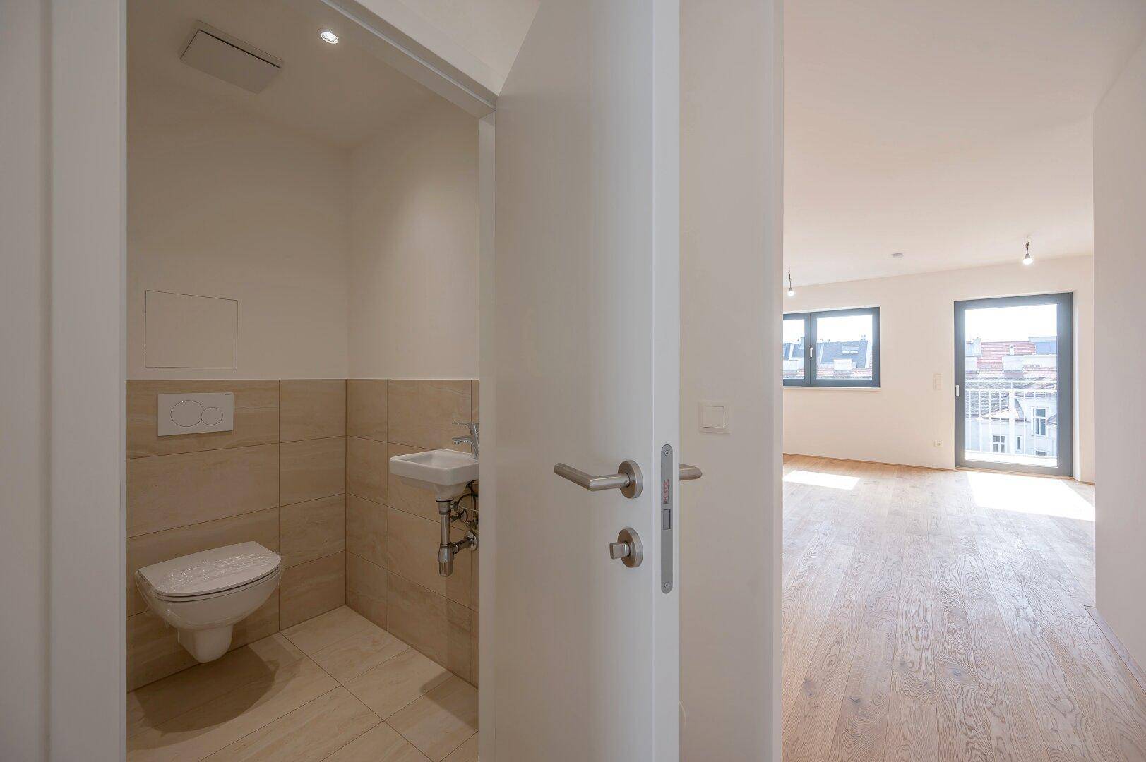 Modernes Gäste-WC mit Wand-WC, kleinem Waschbecken und hellen Fliesen.