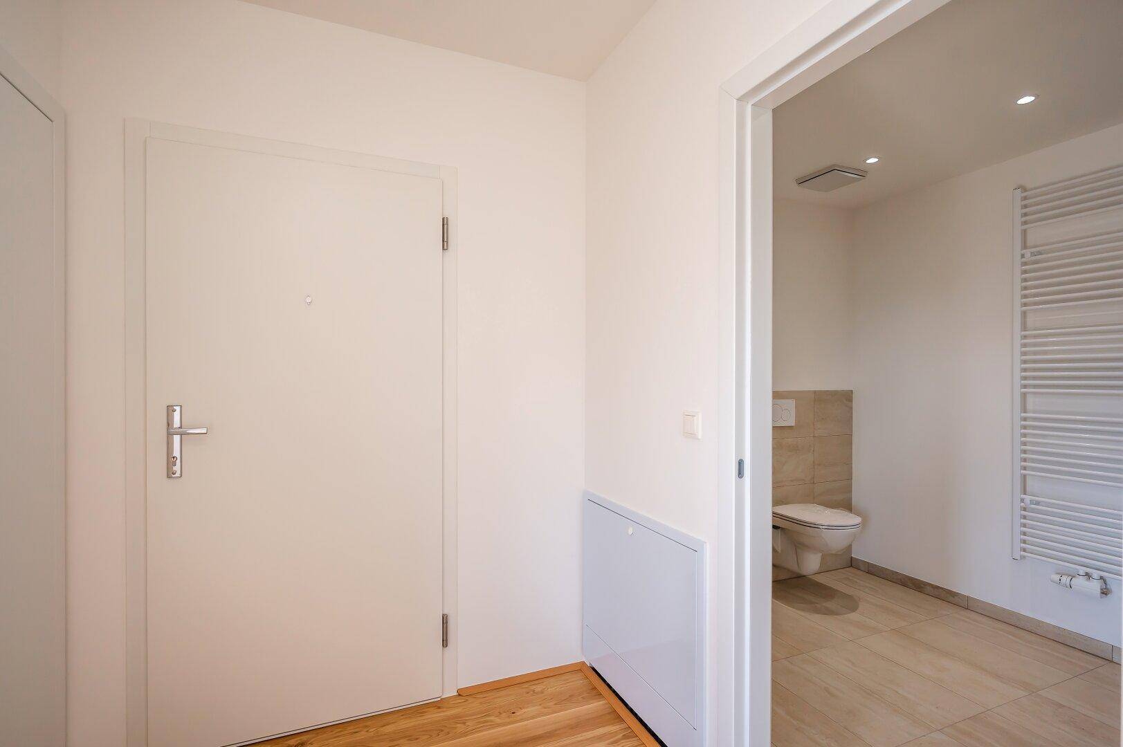 Heller Eingangsbereich mit weißer Tür, führt direkt zu einem modernen Badezimmer.