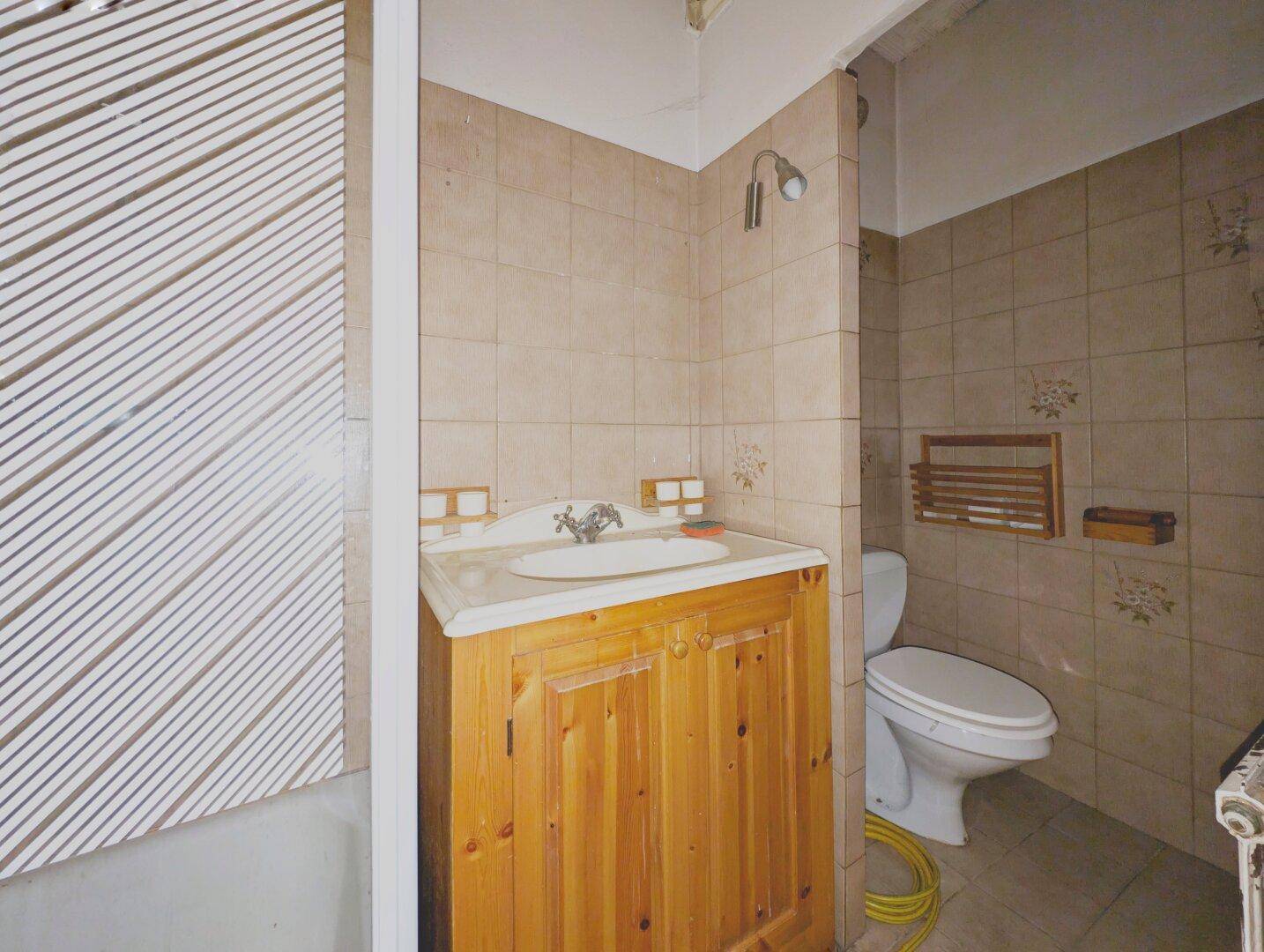 Badezimmer mit beigefarbenen Fliesen, Holzwaschtisch und Toilette, das eine Modernisierung erfordert.