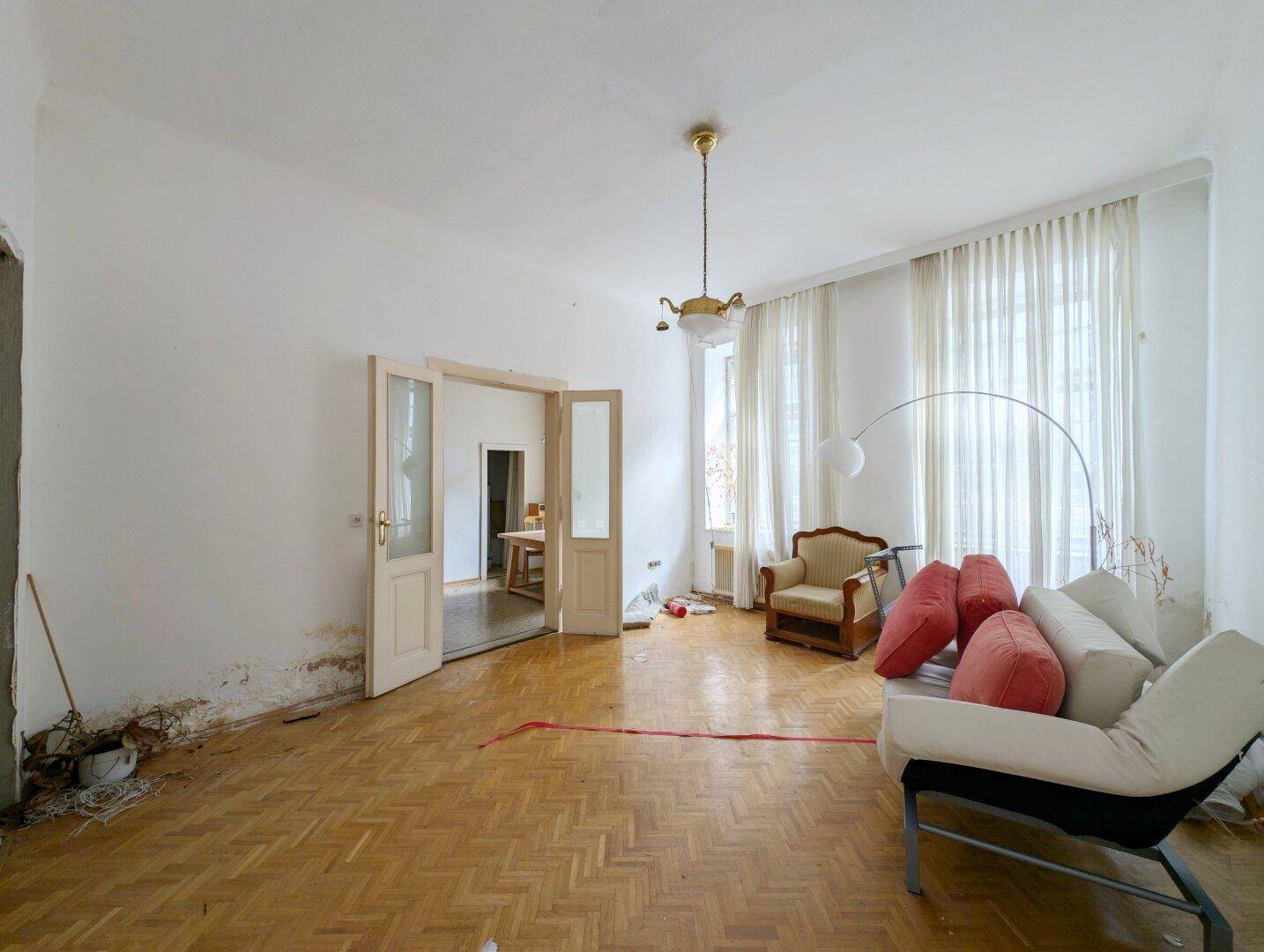 Geräumiges Zimmer mit Fischgrätparkett und hohen Decken, das Renovierungsbedarf aufweist.