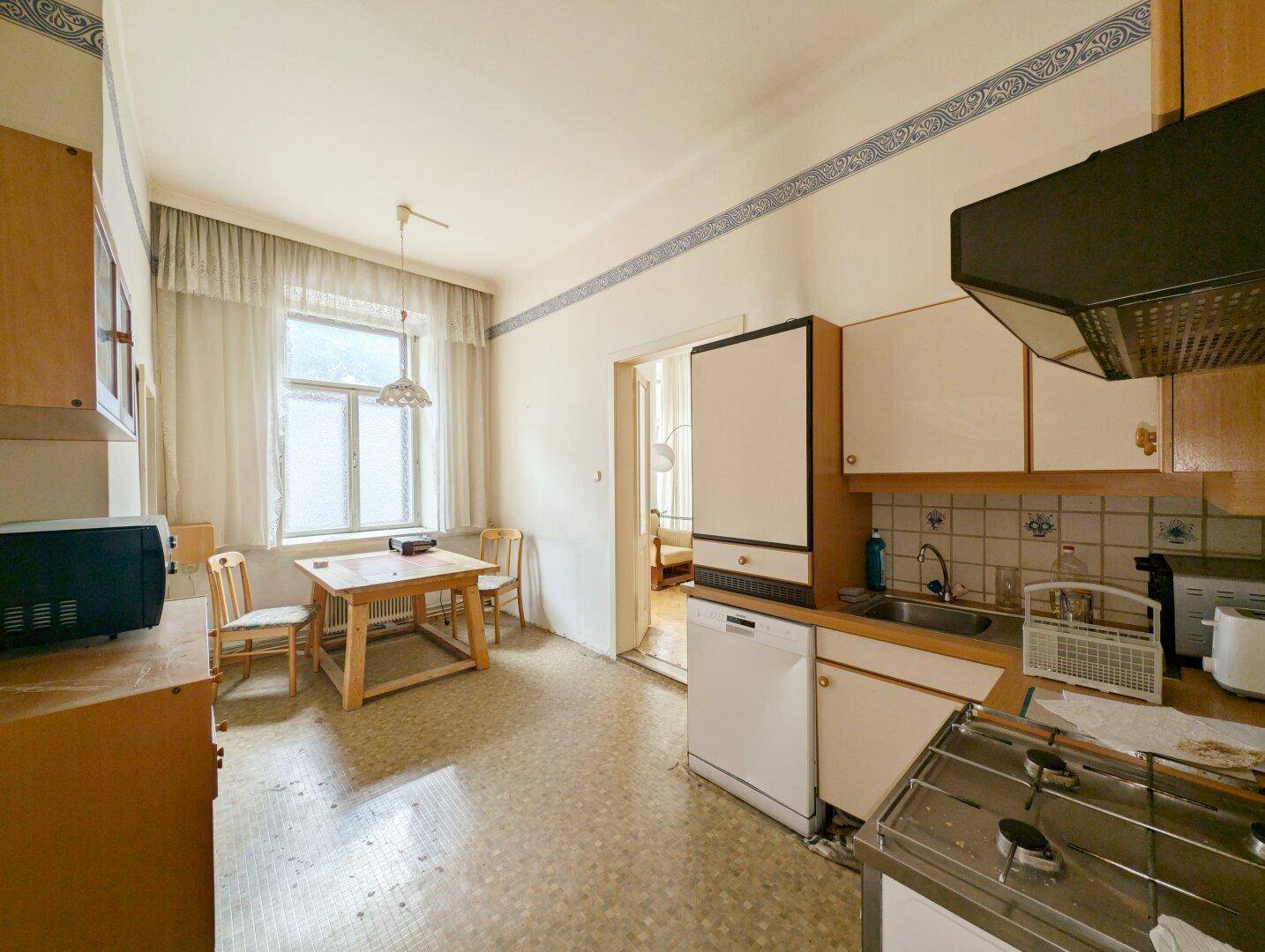 Funktionale Küche mit Essbereich, älteren Einbauten und Terrazzoboden, bereit zur Modernisierung.