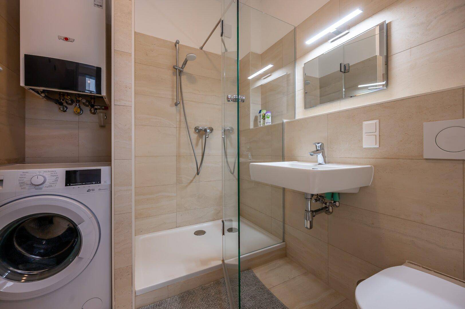 Modernes Badezimmer mit Dusche, Waschbecken, Toilette und integrierter Waschmaschine.