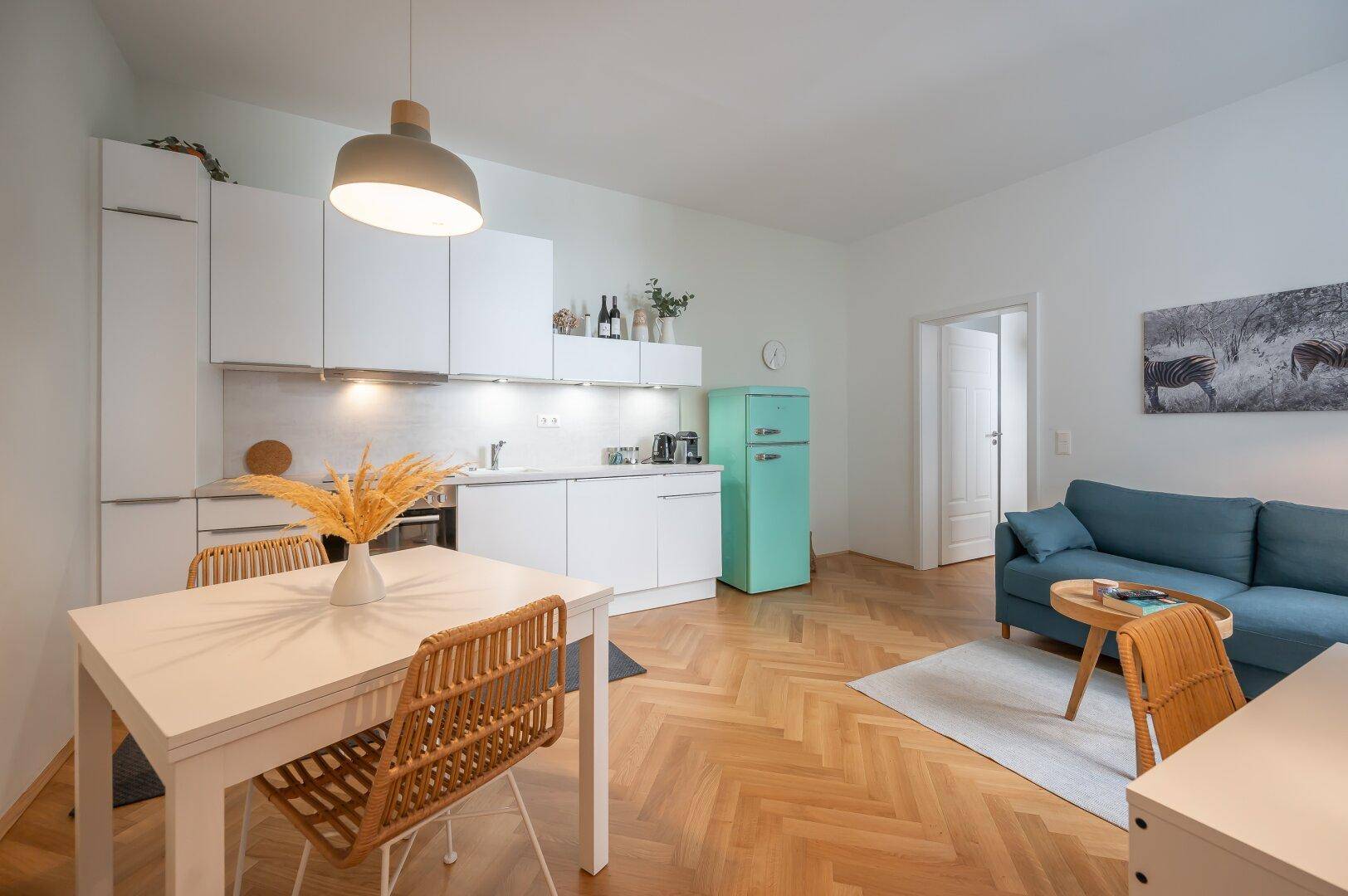 Heller Wohnbereich mit integrierter Küche, Essplatz und gemütlichem Sofa auf Parkettboden.