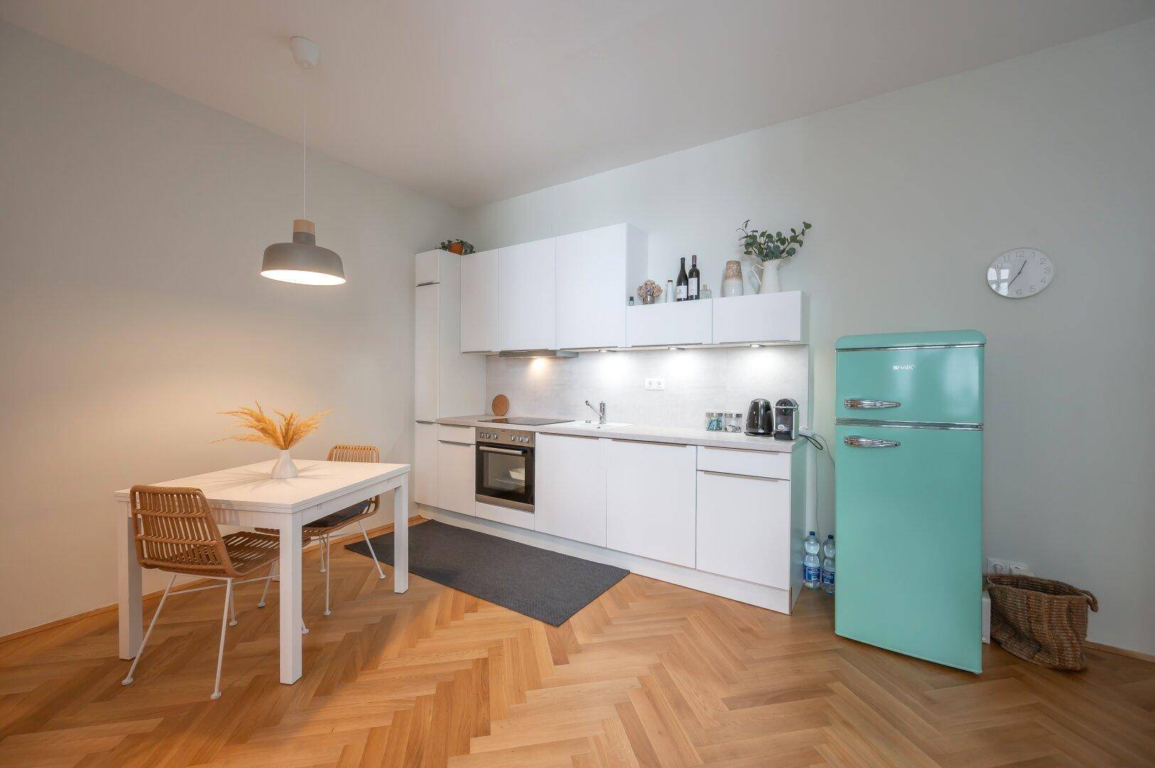 Moderne Einbauküche mit weißer Front, Essbereich und einem auffälligen mintgrünen Kühlschrank.