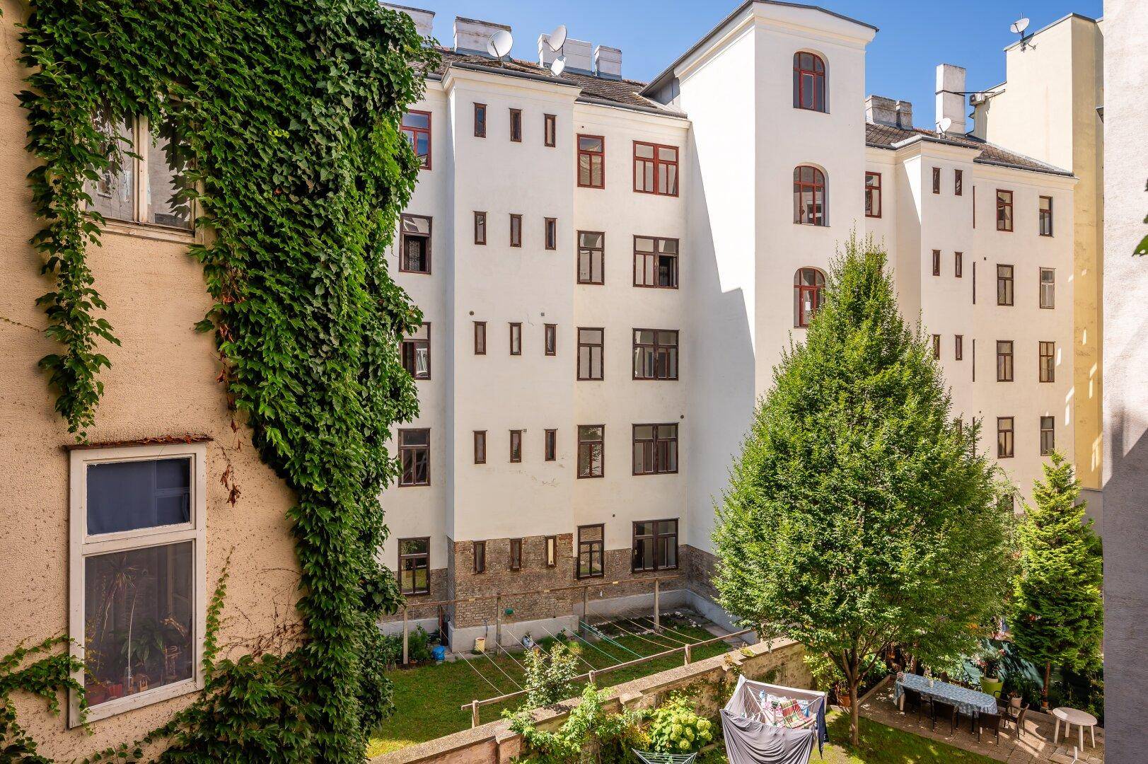 Hinterhofgarten mit Rasenfläche, Bäumen und Gebäudefassade, bietet einen ruhigen Rückzugsort.
