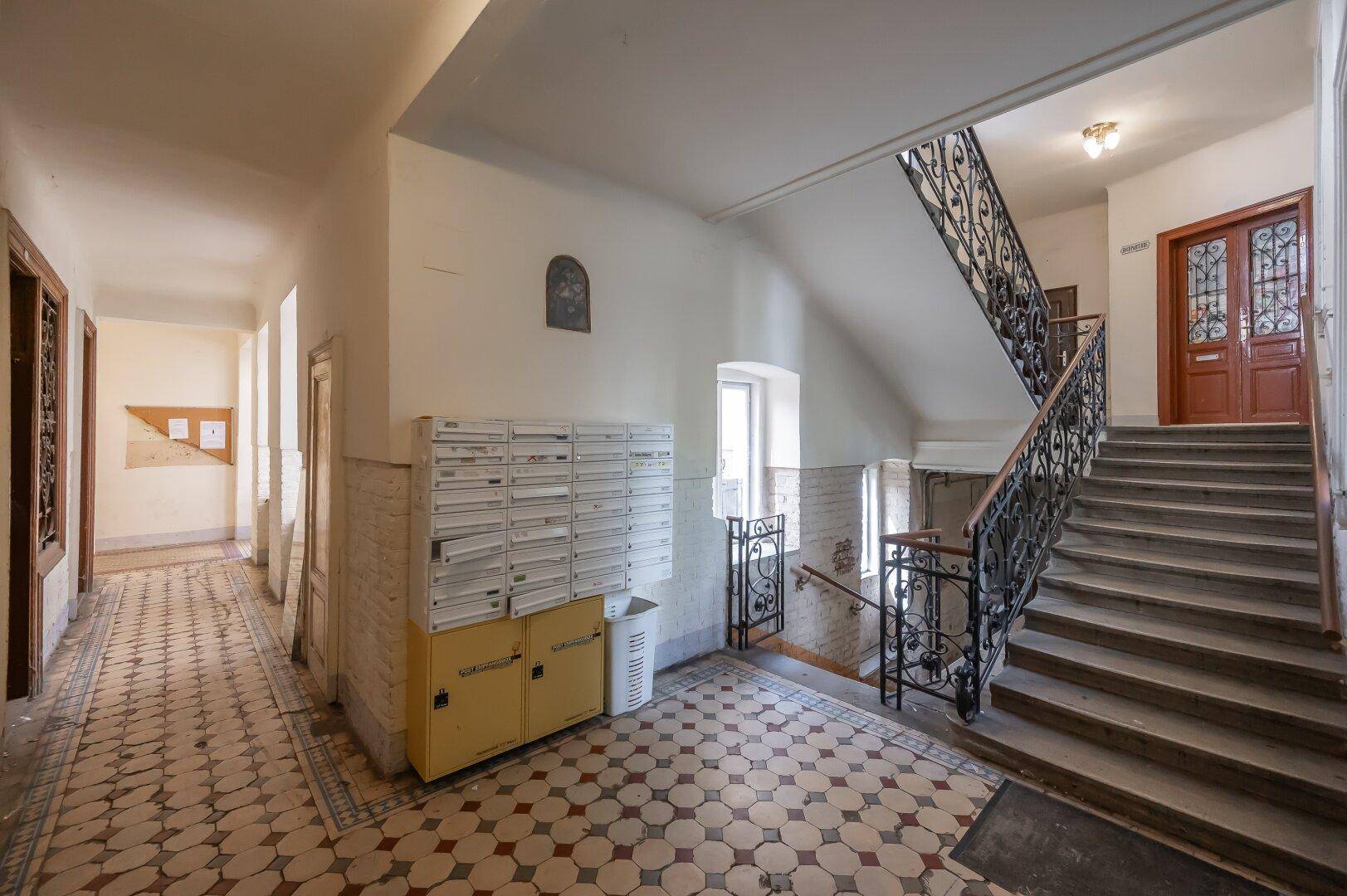 Eingangsbereich eines Mehrfamilienhauses mit Briefkästen, Treppenhaus und gemustertem Fliesenboden.