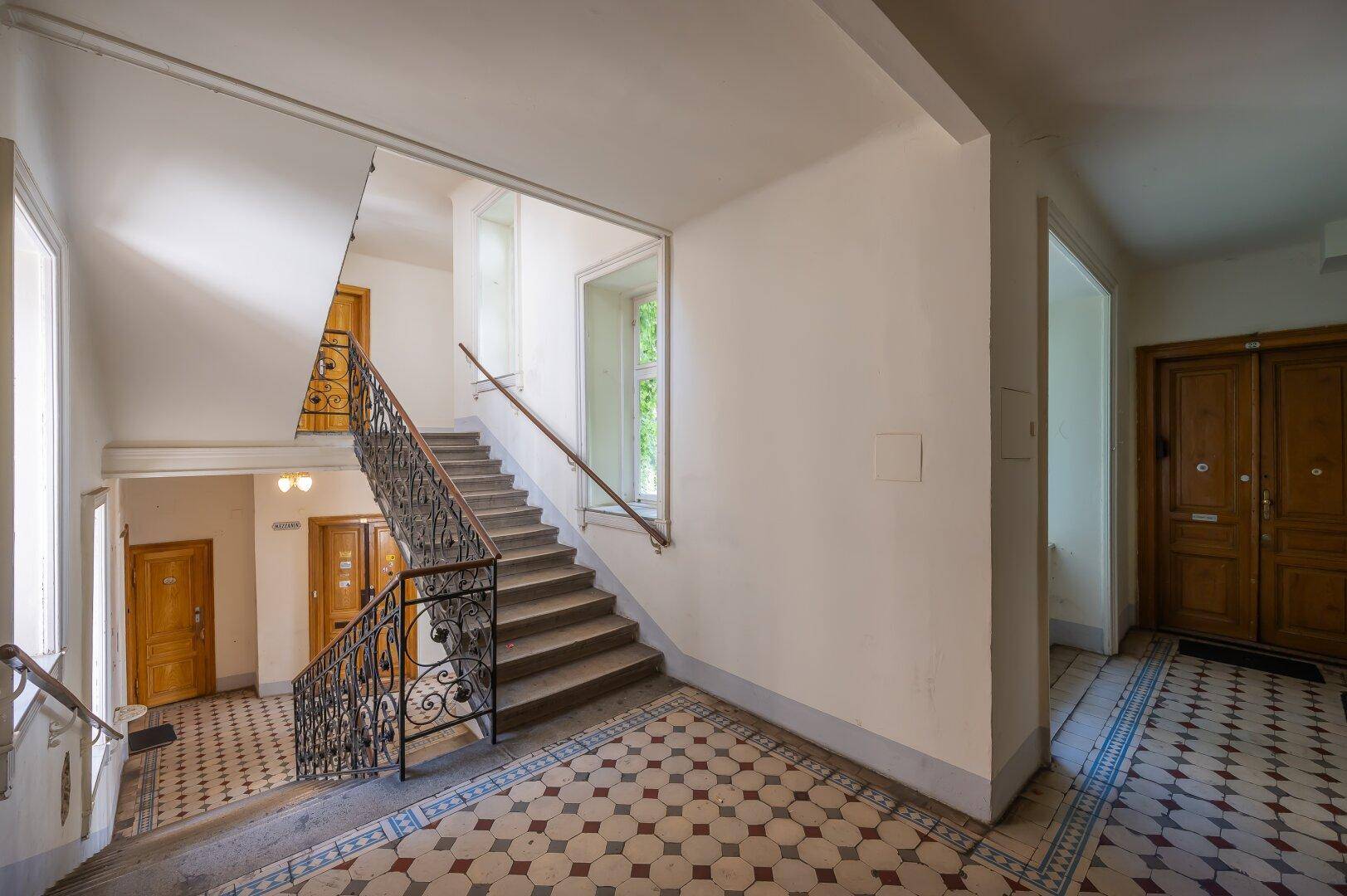 Geräumiges Treppenhaus mit Tageslicht, schmiedeeisernem Geländer und gemustertem Fliesenboden.