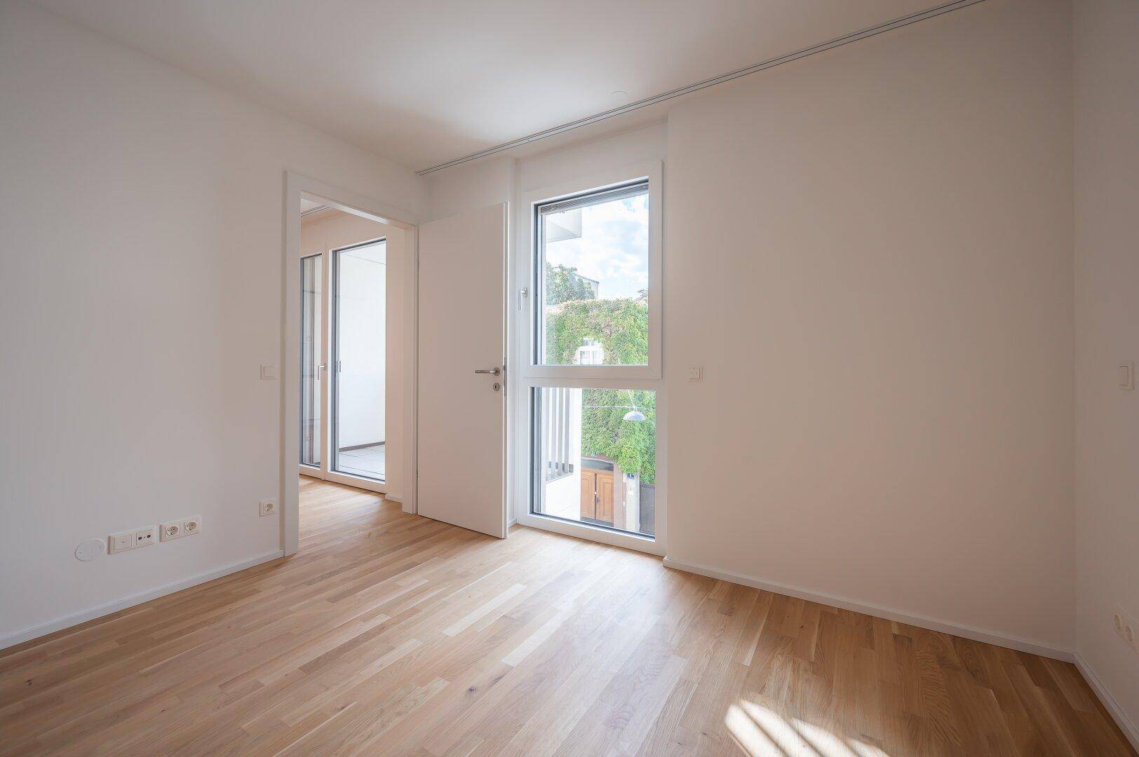 Helles Zimmer mit Holzboden, großen Fenstern und Zugang zu einem französischen Balkon.