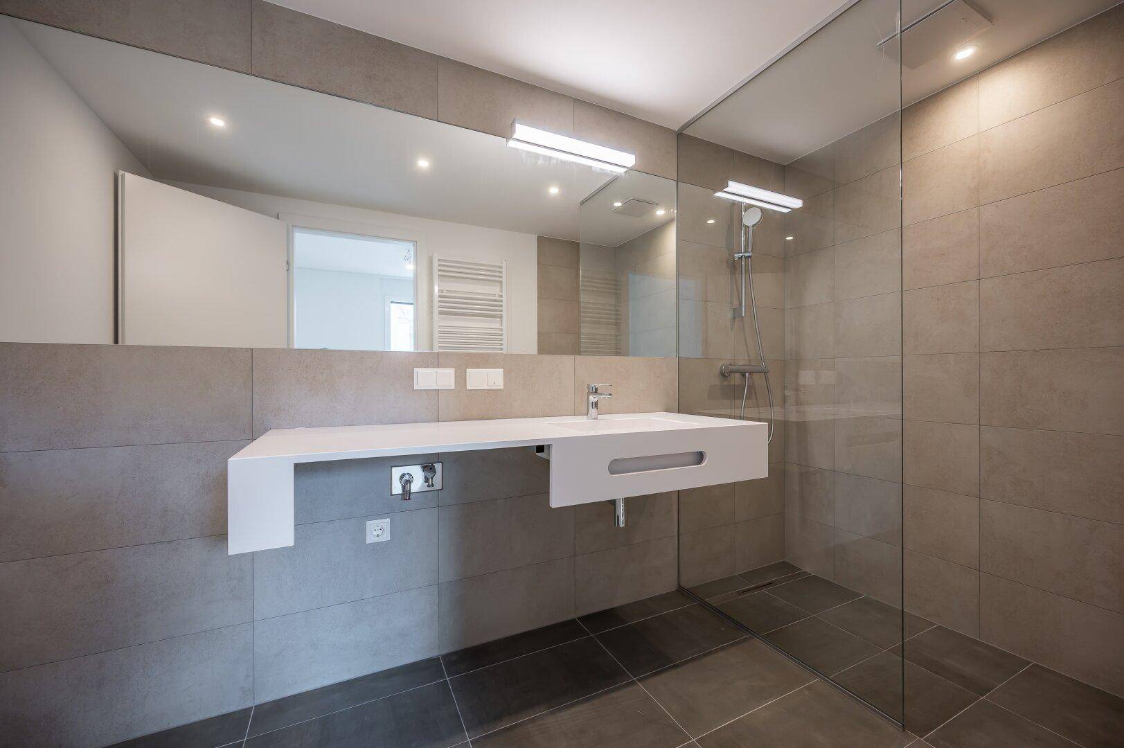 Modernes Badezimmer mit großer Spiegelfläche, Waschtisch und ebenerdiger Dusche.