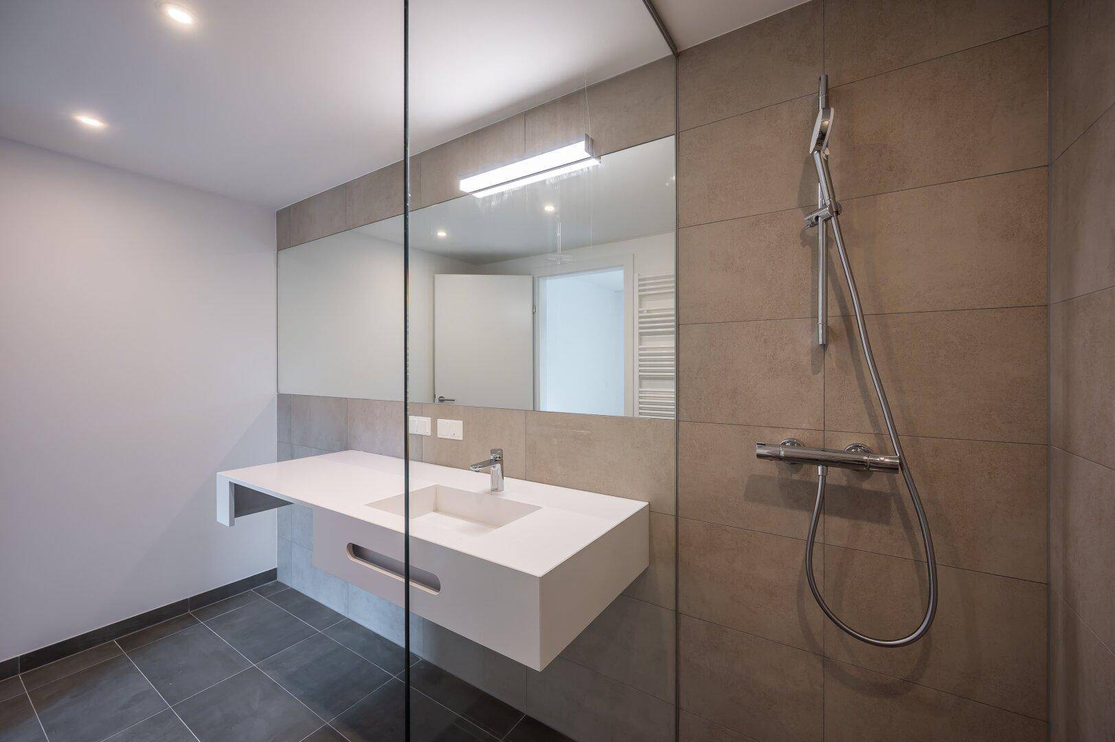 Elegantes Badezimmer mit großem Spiegel, modernem Waschtisch und Glasdusche.