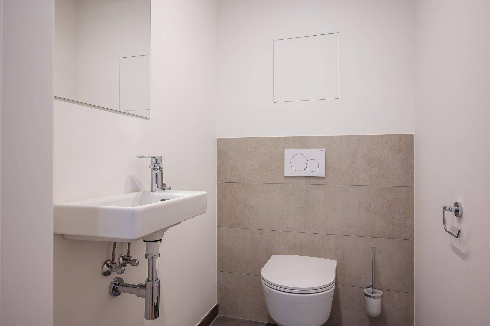 Moderne Gästetoilette mit Wand-WC, kleinem Waschbecken und grauen Fliesen.