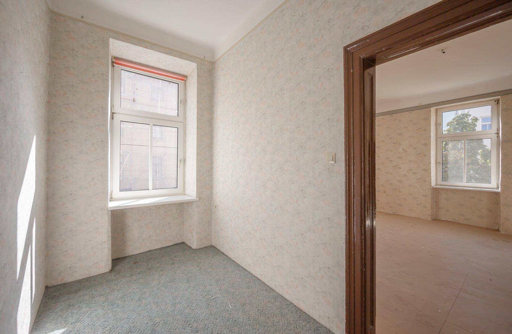 Leerer Raum mit gemusterter Tapete, Teppichboden und Fenster, bereit zur Neugestaltung.