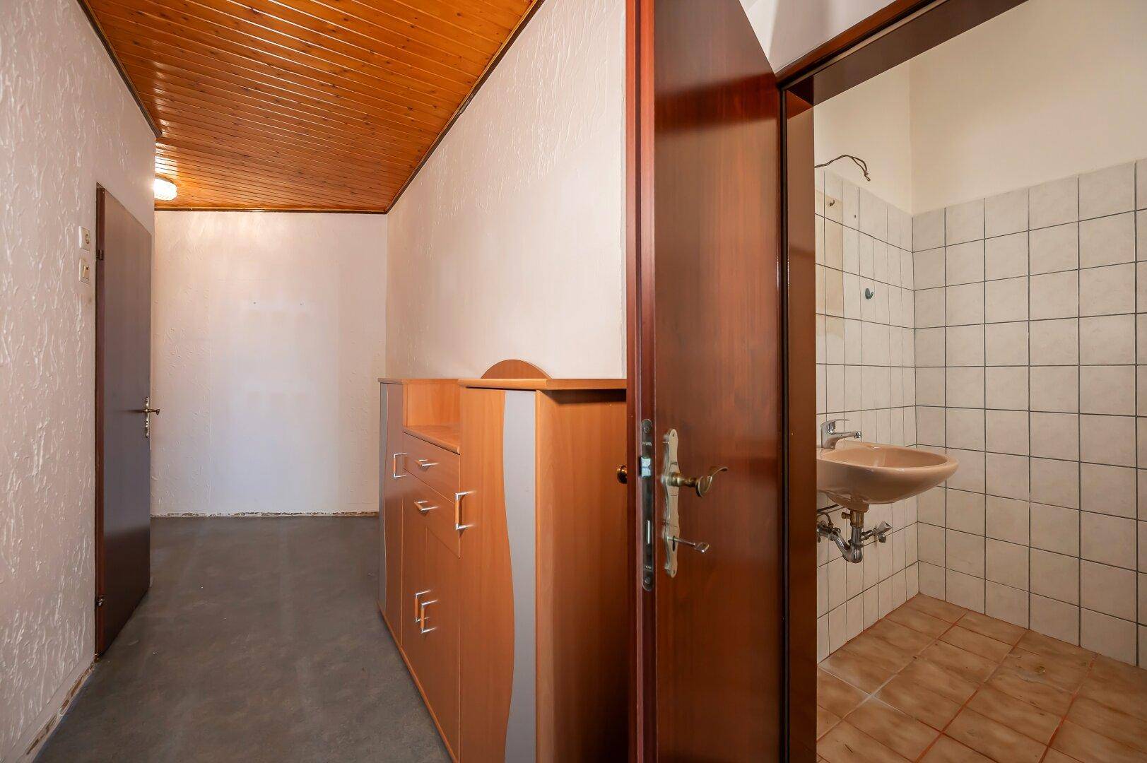 Flur mit Holzdecke und Schrank, der zu einem Badezimmer mit Waschbecken führt.