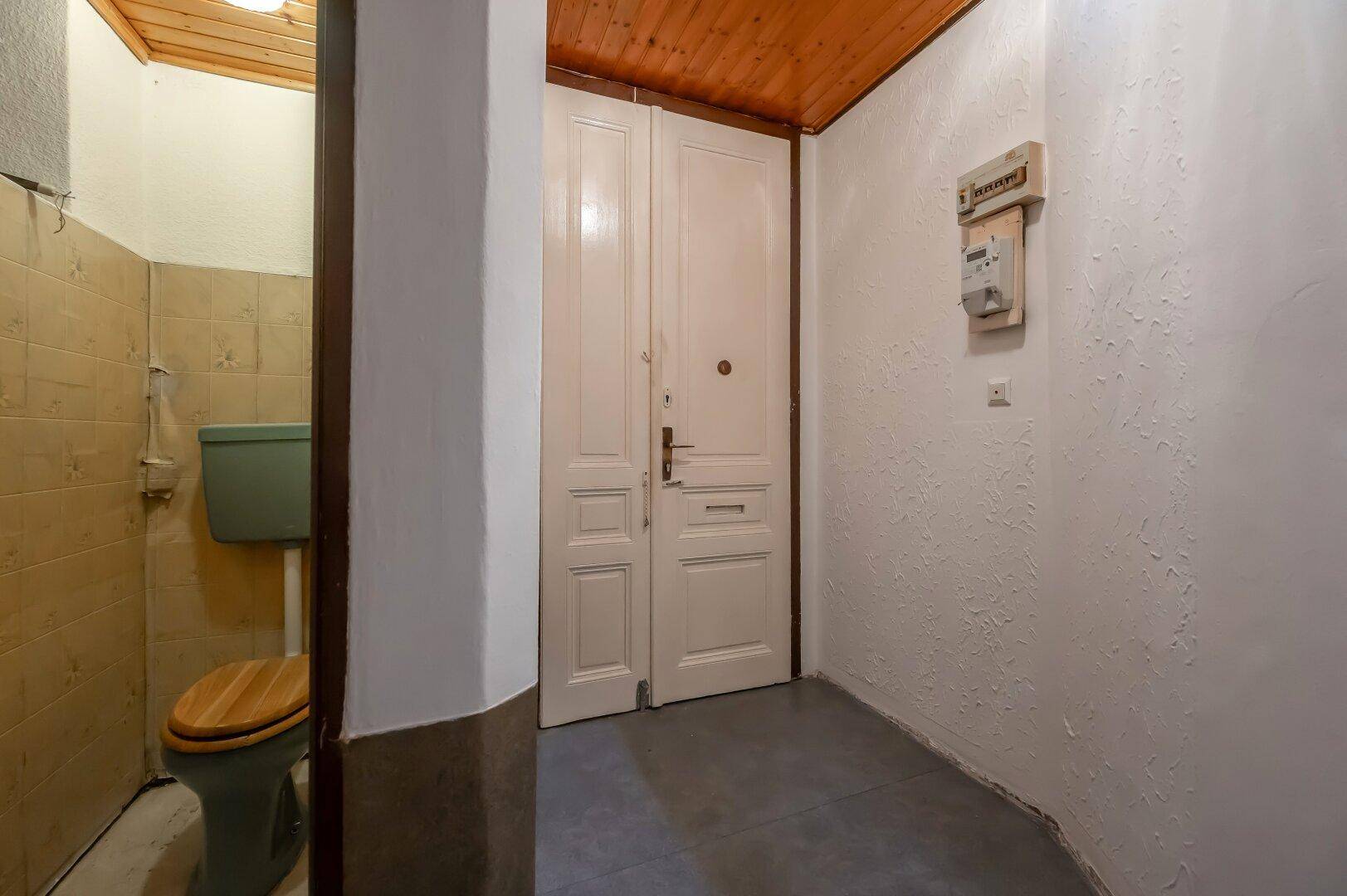 Kleiner Toilettenbereich mit gefliesten Wänden, Holzdecke und einfacher Ausstattung.