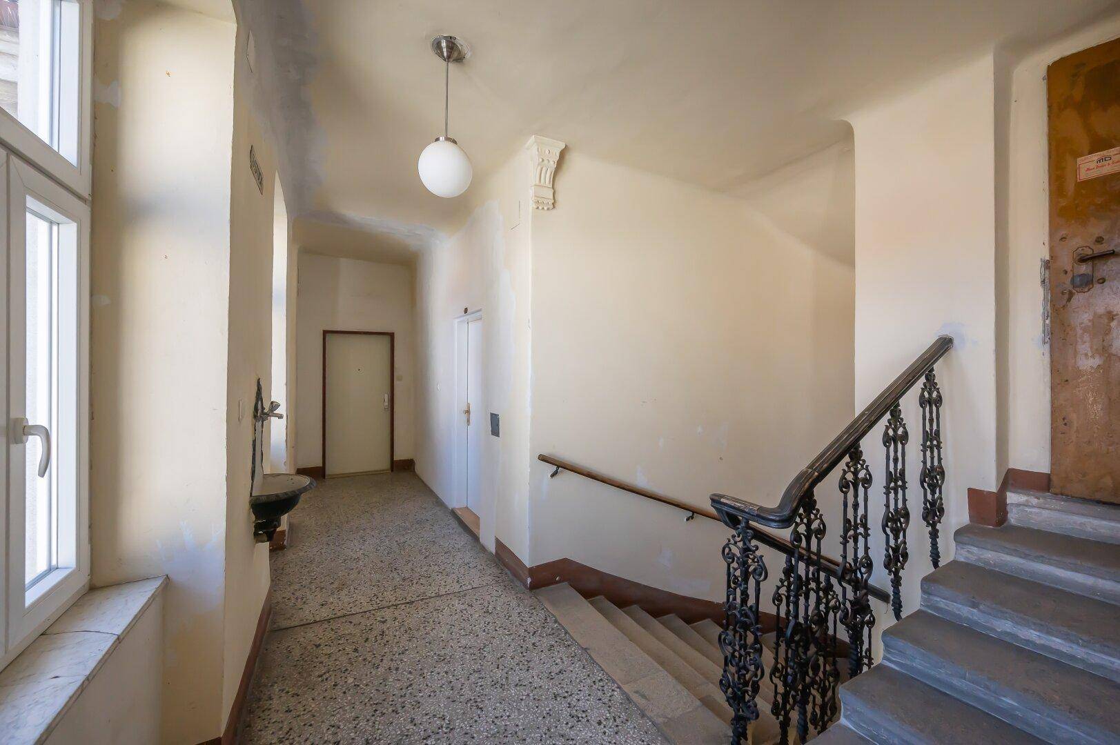 Treppenhaus und Flur eines Altbaus mit Terrazzoboden und schmiedeeisernem Geländer.