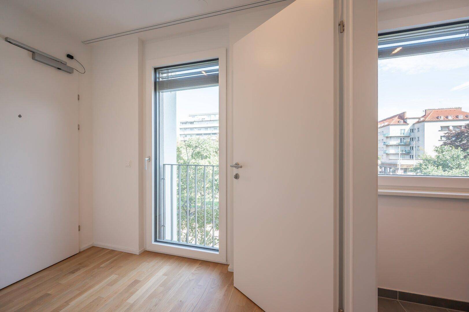 Helles Zimmer mit französischem Balkon und Blick auf die umliegende Bebauung.