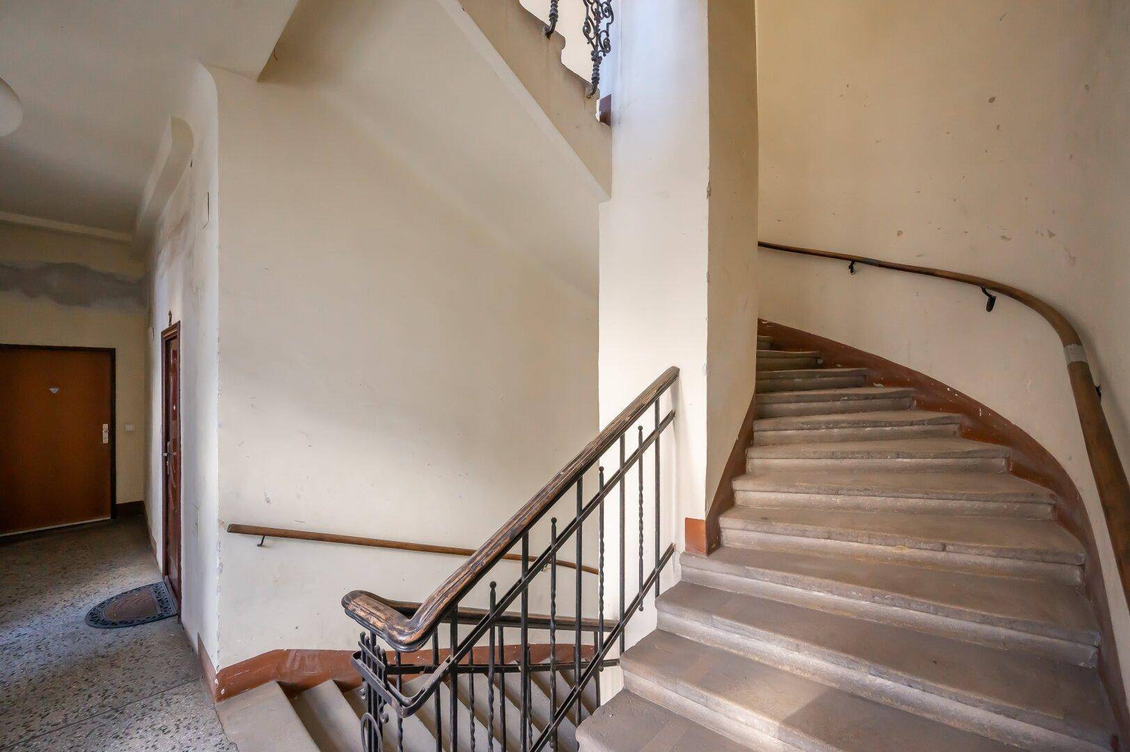 Historisches Treppenhaus mit geschwungener Form, schmiedeeisernem Geländer und Holzhandlauf.