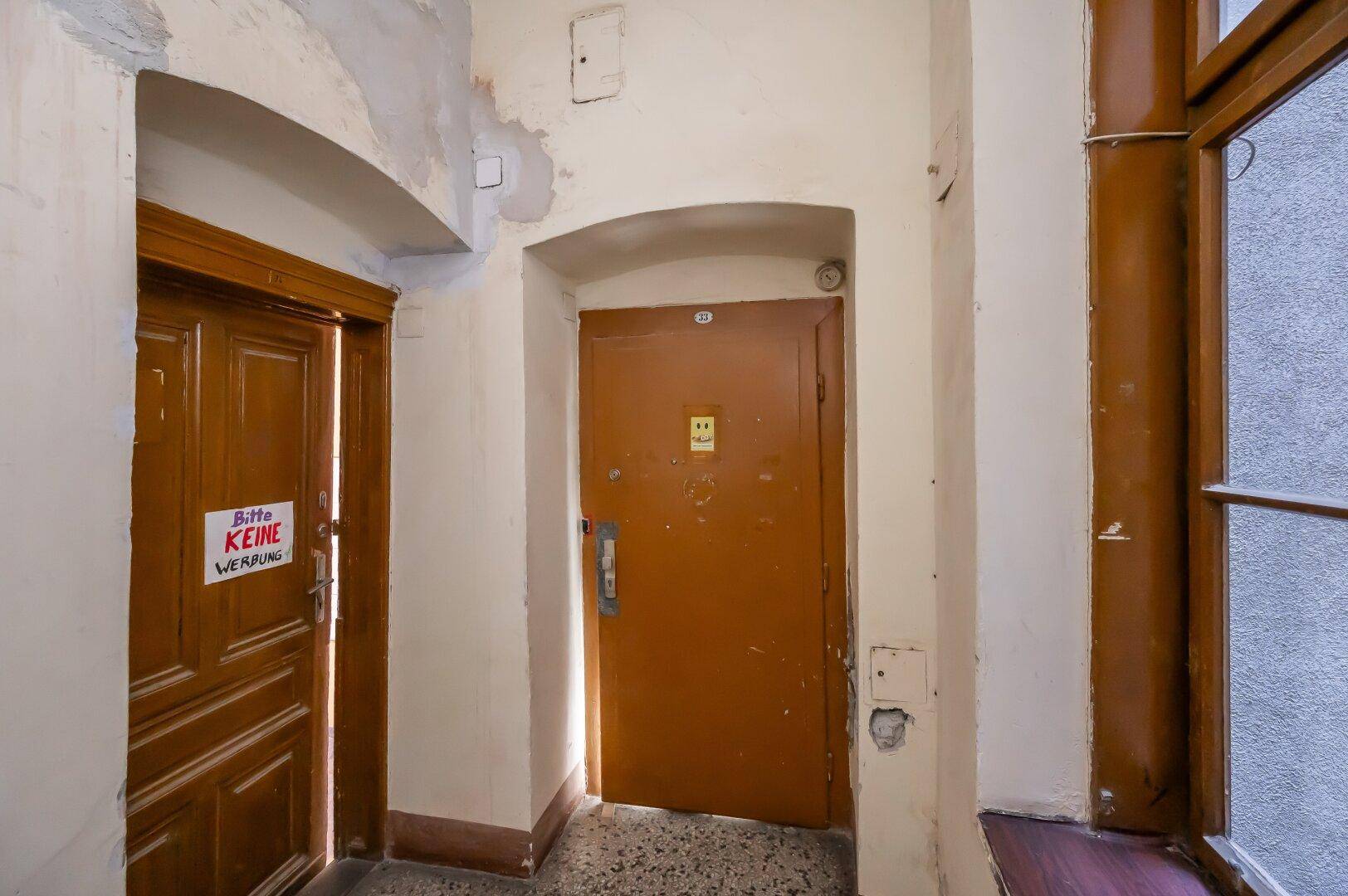 Alter Flur mit zwei Holztüren und einem Fenster, das Tageslicht hereinlässt.