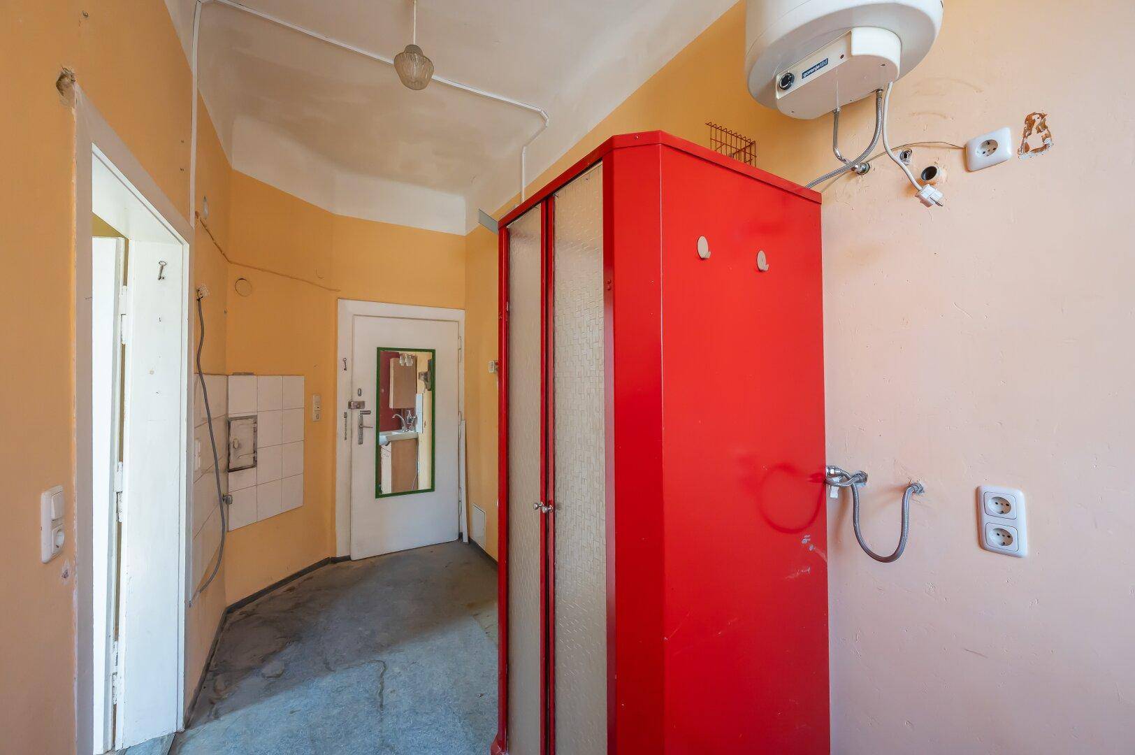 Badezimmer mit rotem Schrank, Warmwasserbereiter und Zugang zu einem weiteren Raum.