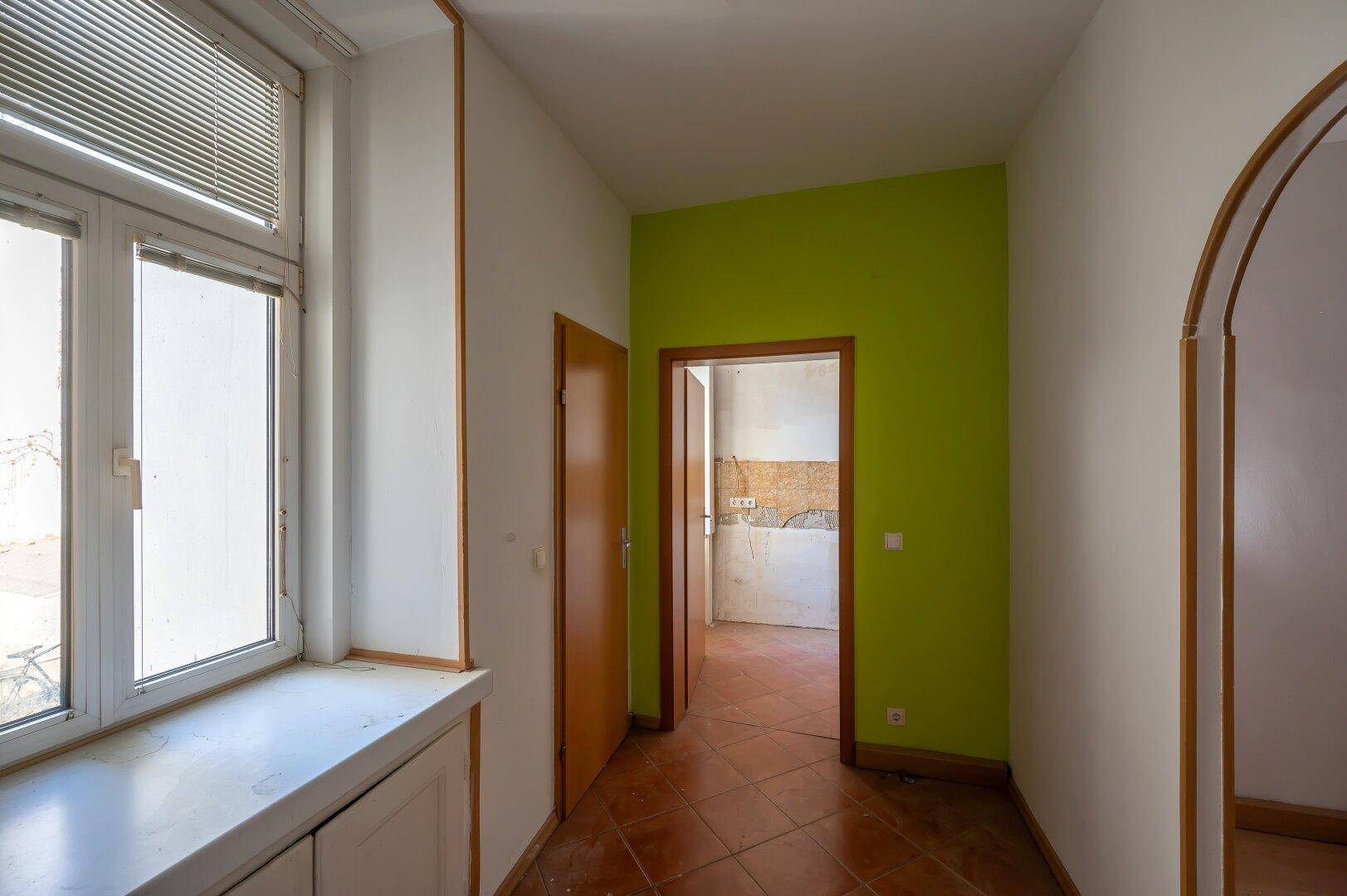 Flur mit Terrakottafliesen und grün gestrichener Wand, führt zu weiteren Räumen.